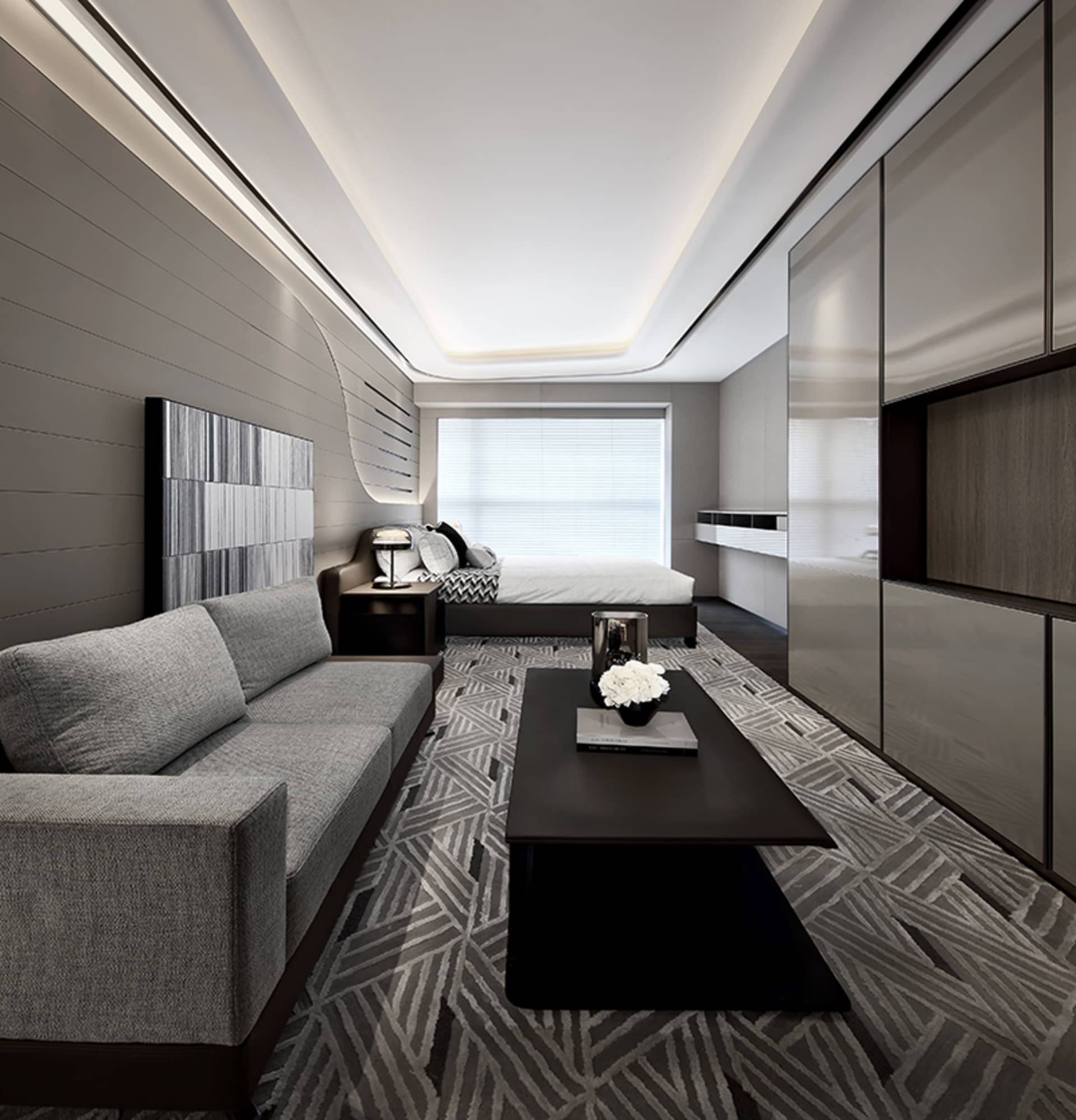 A modern minimalist bedroom featuring a grey couch, a black coffee table with white flowers, and a neatly made bed.