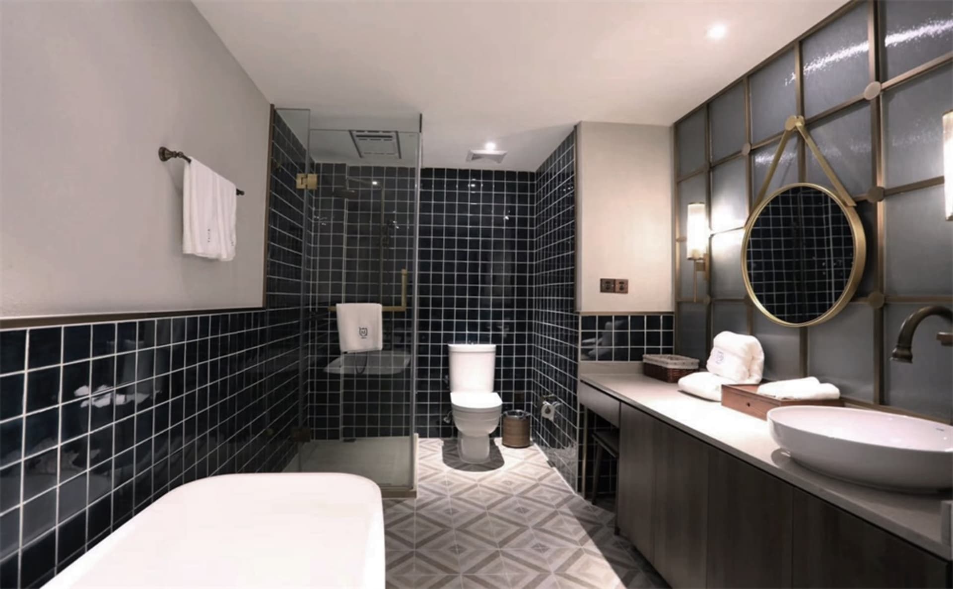 Modern bathroom featuring black tiles in a geometric pattern, with a freestanding bathtub, a toilet, a vanity with a white si