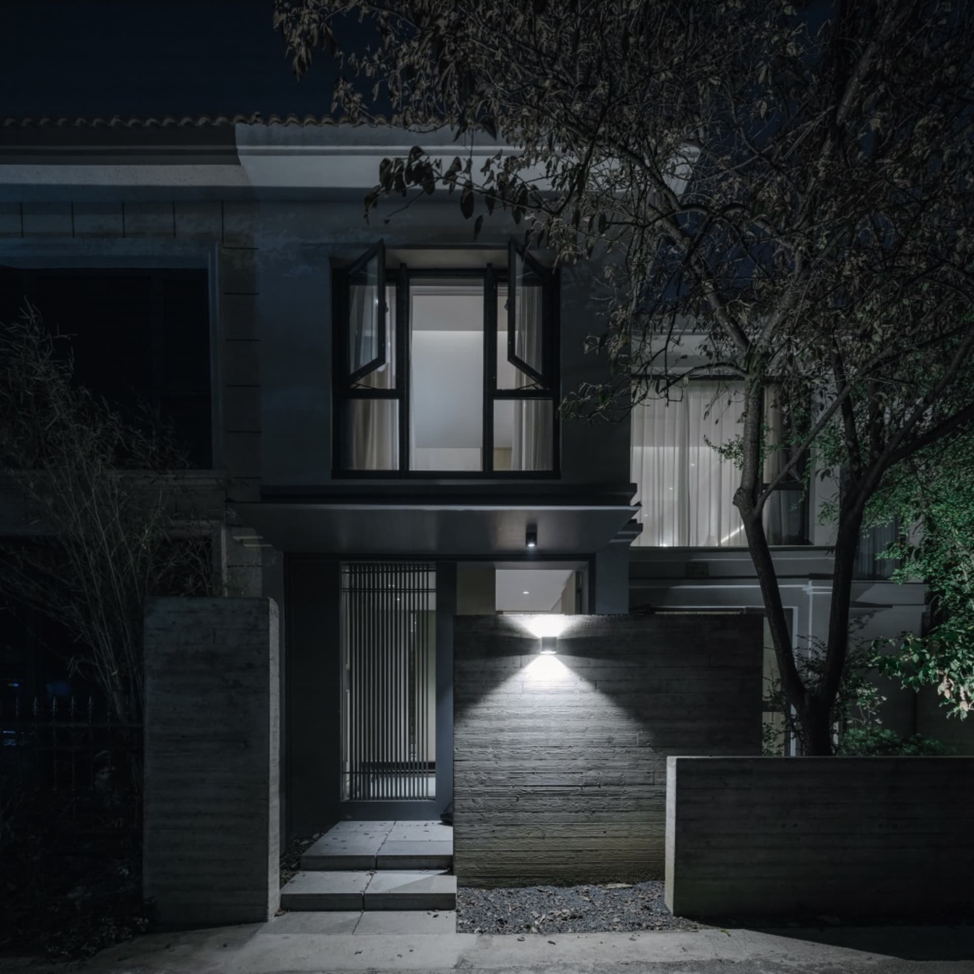 A modern house facade made of concrete with lights illuminating the entrance.