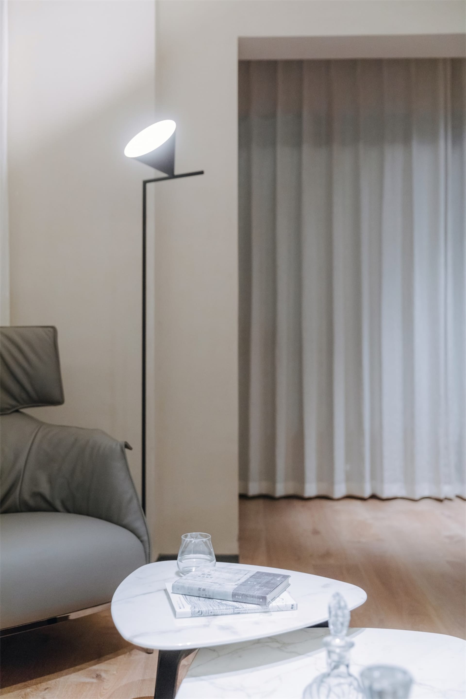 A modern living room featuring a grey leather sofa, a triangular marble coffee table, and a black floor lamp with a white sha