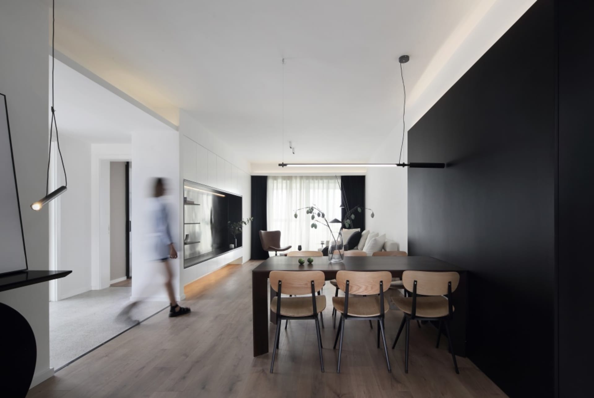 A modern minimalist living room with black walls, wooden furniture, and glass elements.