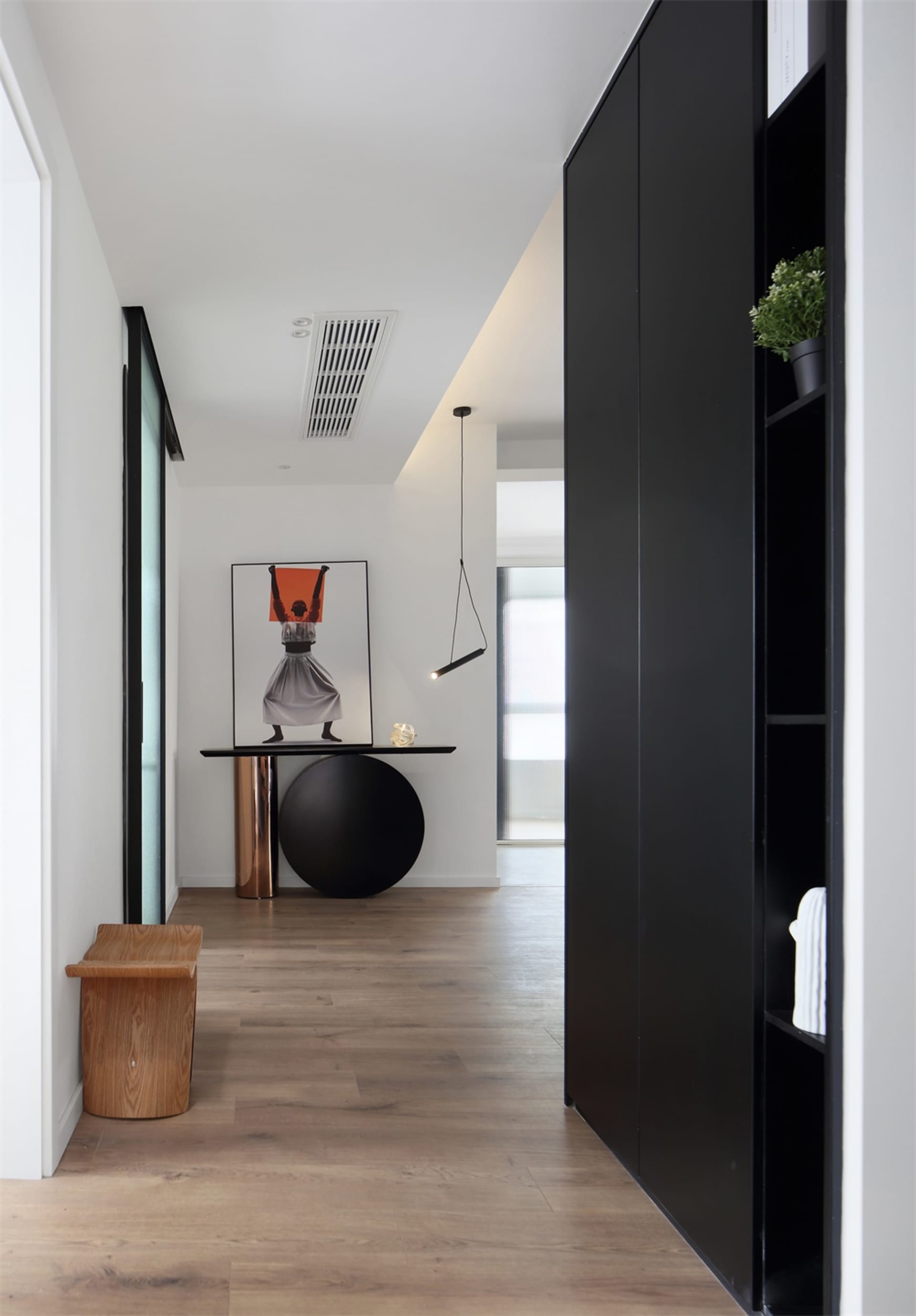 A modern interior design corridor with wooden flooring, a black table, and a black lamp hanging from the ceiling.