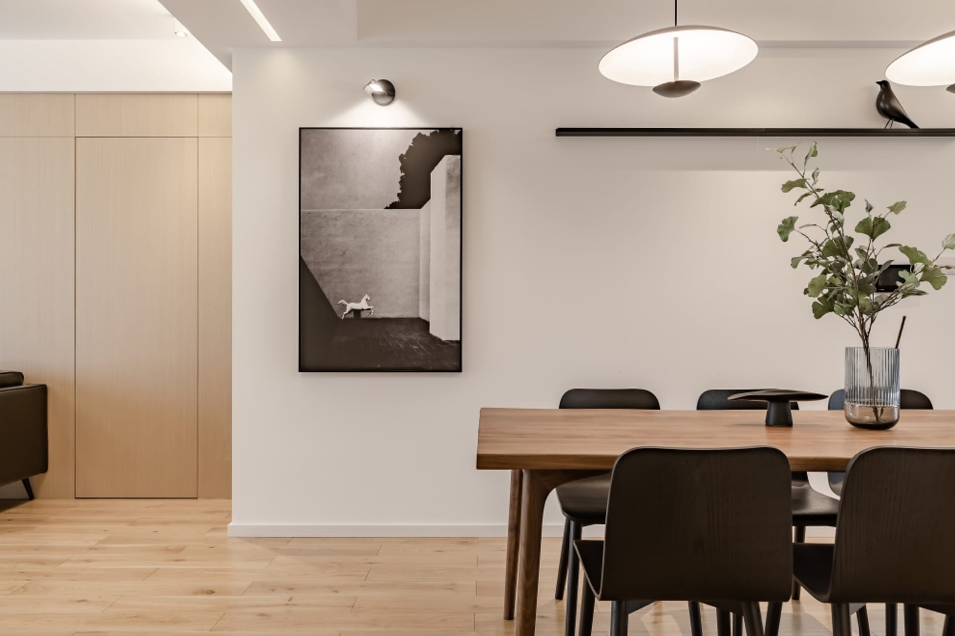 Modern minimalist dining room featuring a wooden table and chairs, with a black and white photograph of a horse on the wall.