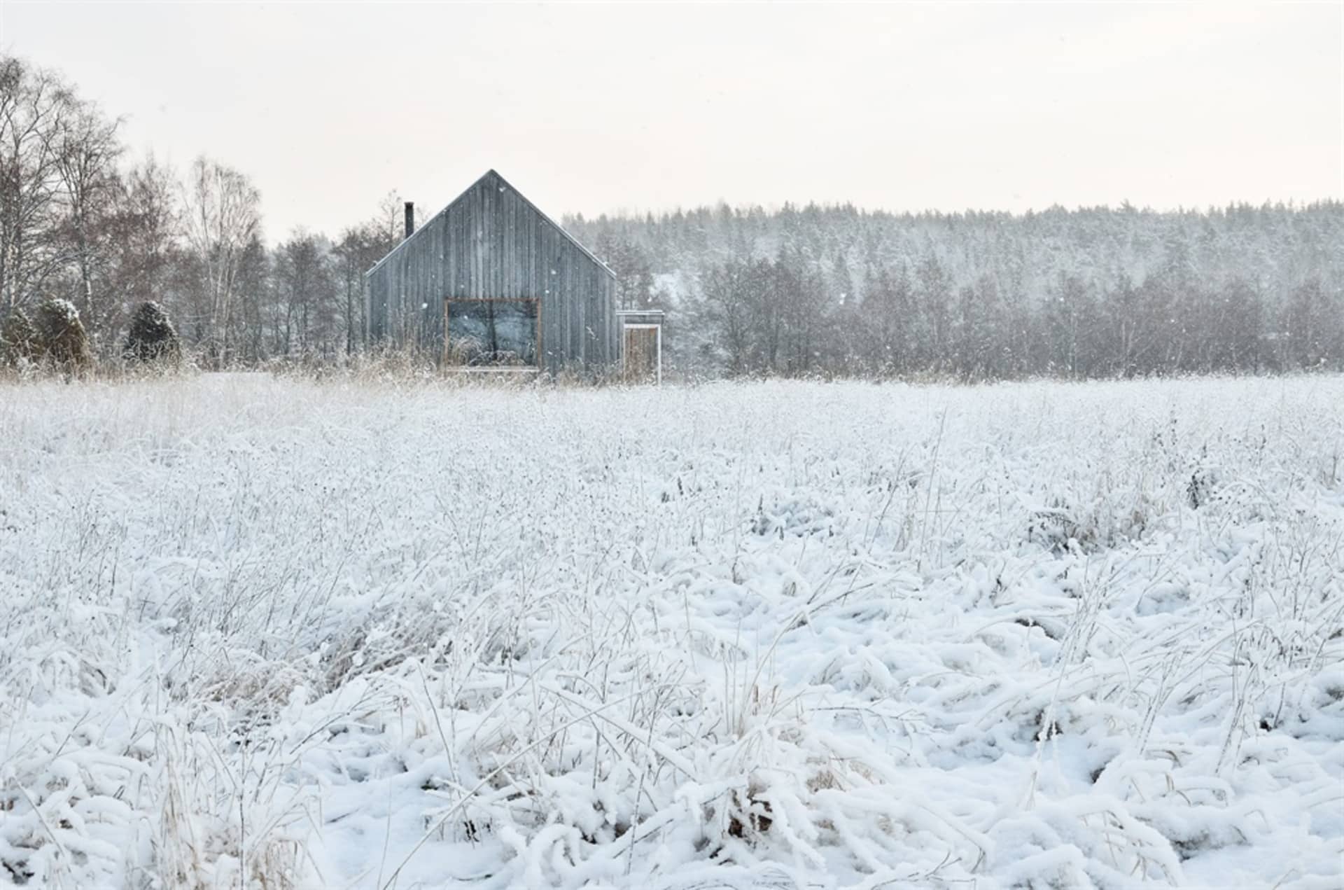 A rustic cabin covered in snow surrounded by a snowy landscape and trees in the background.