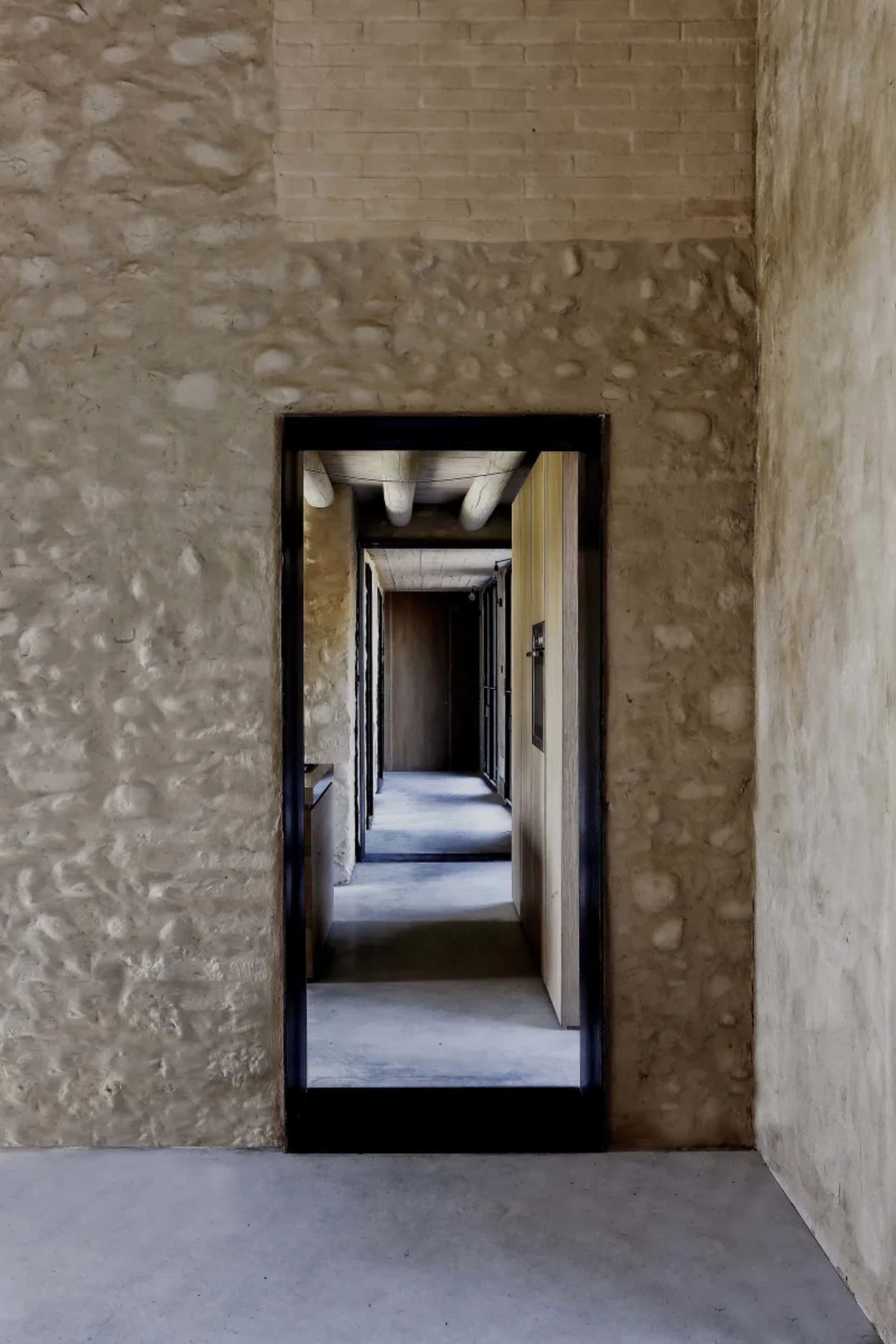 A modern corridor features concrete and brick walls with a stone accent, leading to a hallway with a wooden floor and a stone