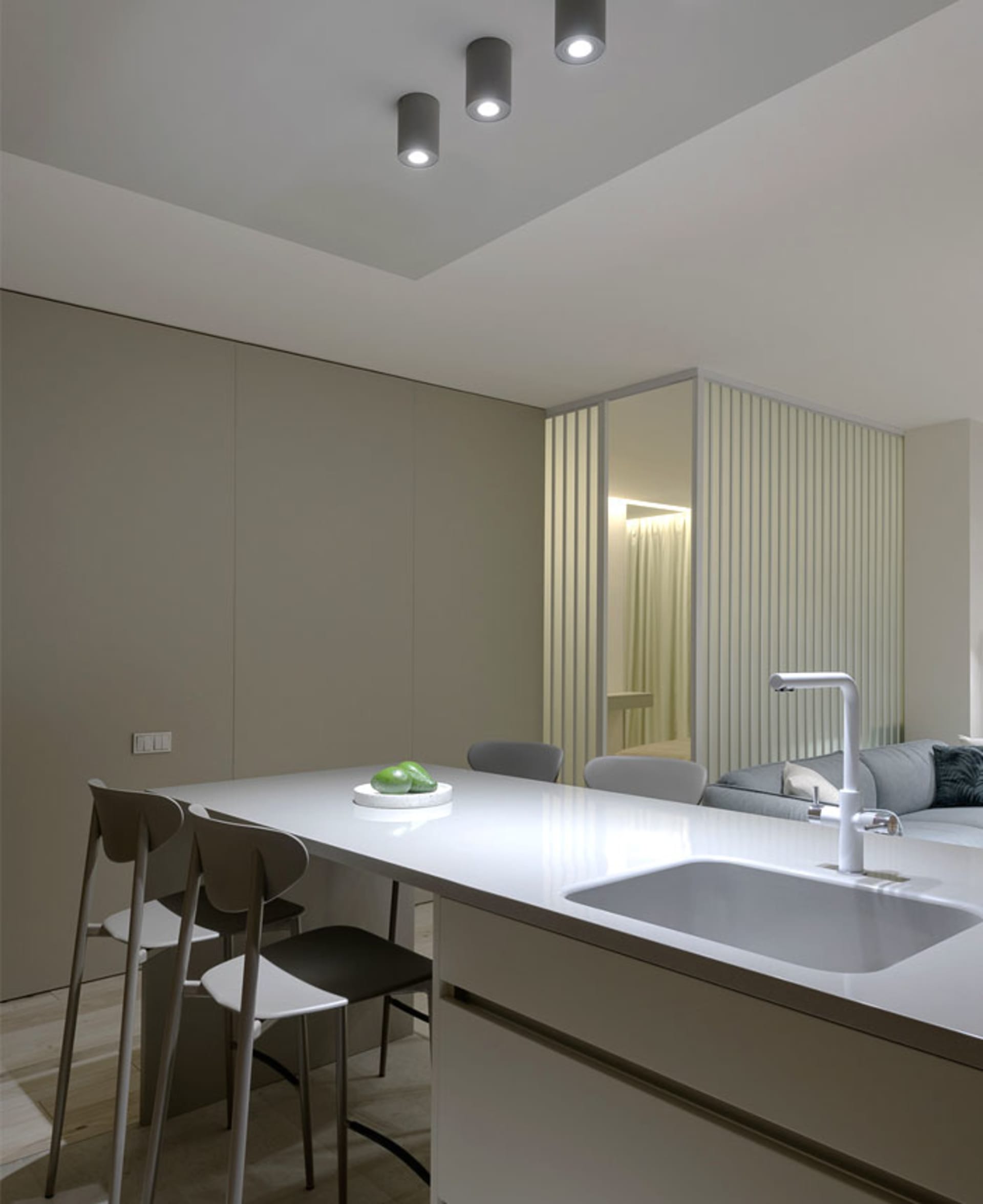A minimalist residential kitchen featuring a white marble countertop with a built-in sink and three stools.