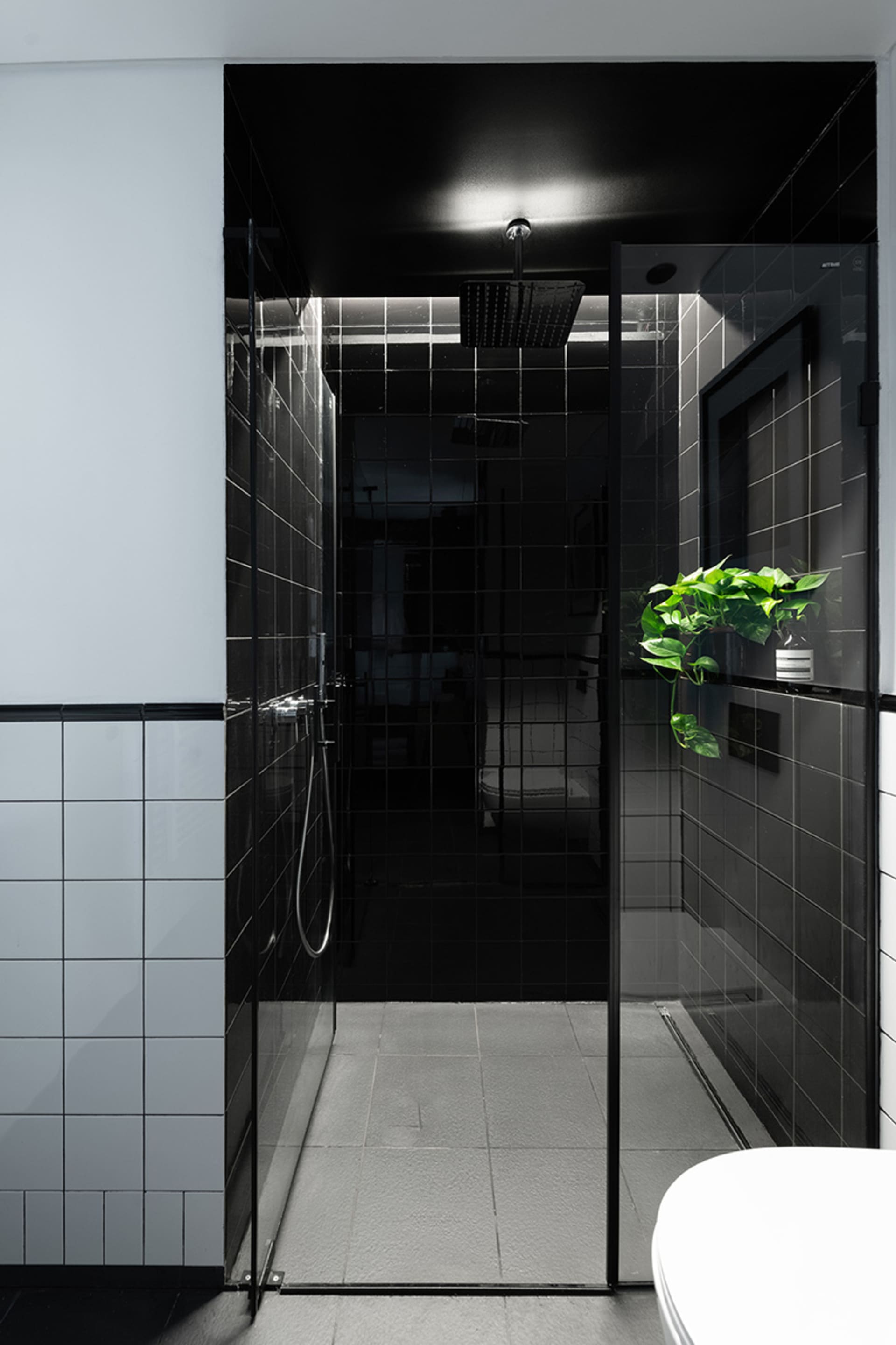 A sleek modern bathroom with black tiled walls and a glass shower enclosure, featuring a white toilet in the foreground and a