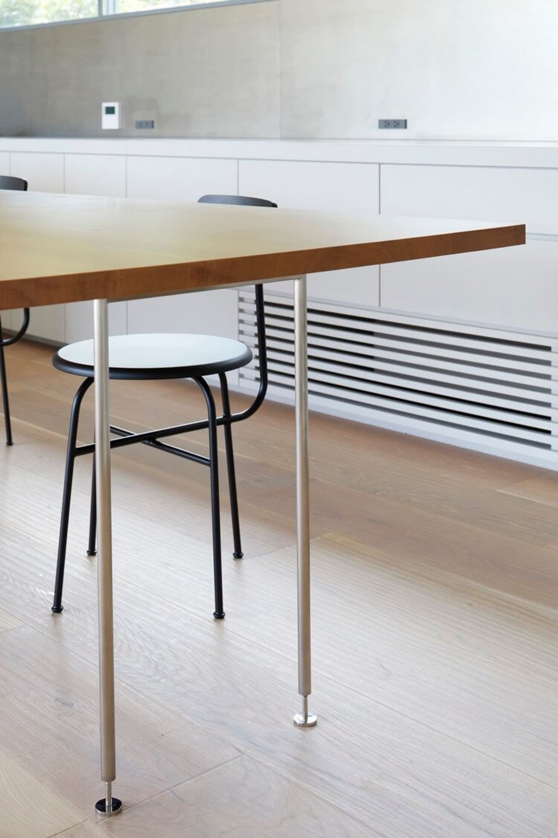 A minimalist office setup featuring a sleek, wooden table and black metal stools.