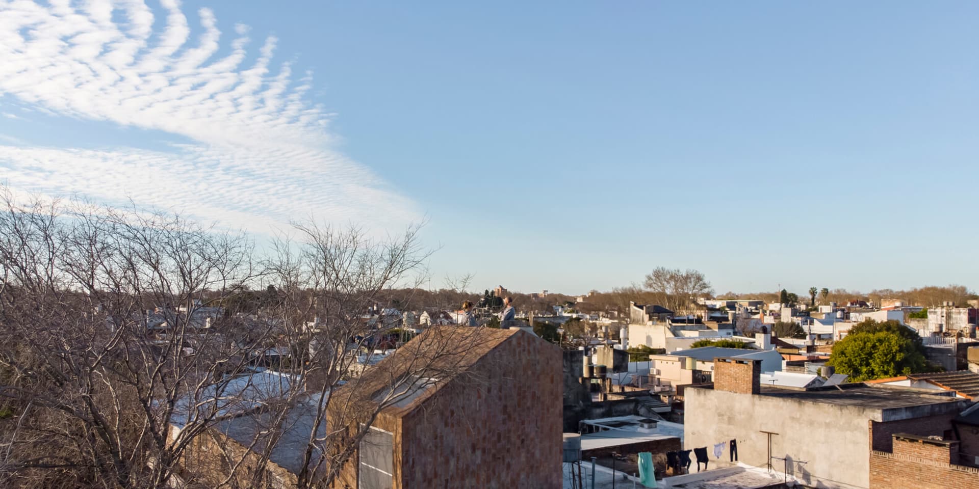 A view of a cityscape featuring brick rooftops and a clear blue sky with scattered clouds.