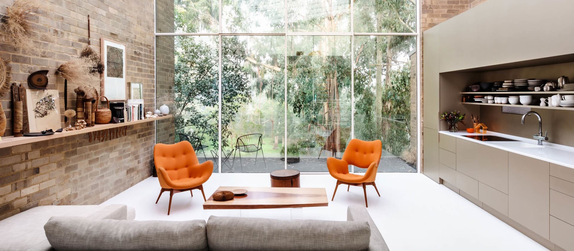 A modern living room featuring a grey sofa, orange chairs, and a concrete and brick wall.