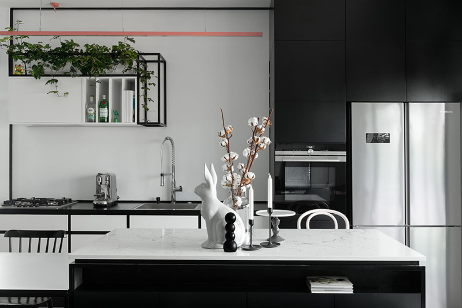 Modern kitchen with minimalist design featuring white marble countertops, black cabinets, and green plants hanging from the c