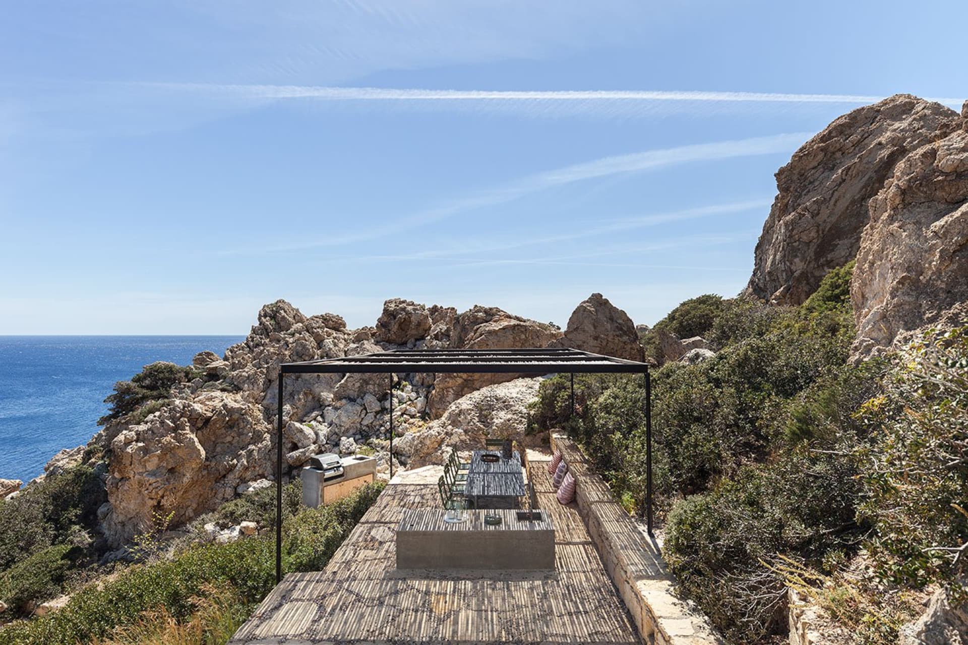 A minimalist outdoor seating area with a table and chairs on a wooden deck overlooking the sea.
