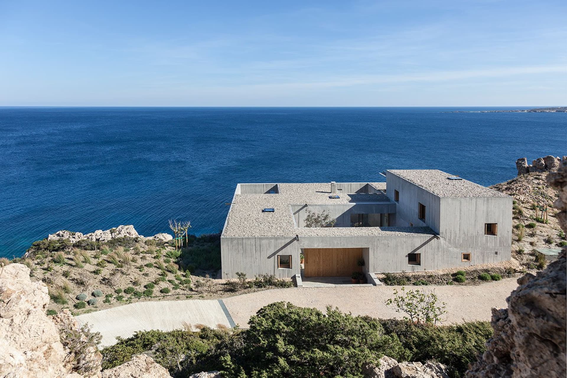 A modern residential house built on a rocky cliff overlooking the sea.