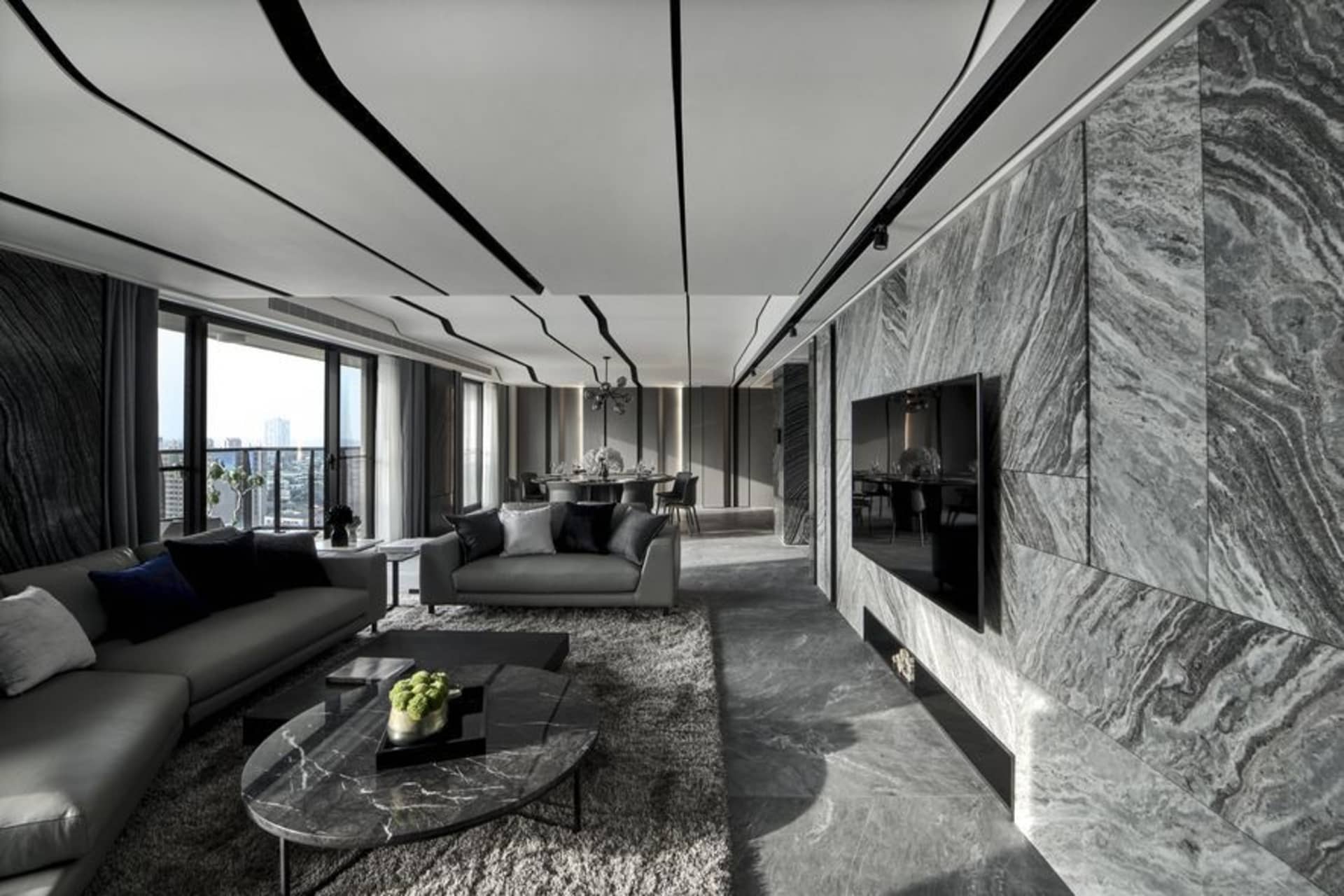 A modern living room featuring a marble wall, ceiling details, and a grey sofa with a marble coffee table.