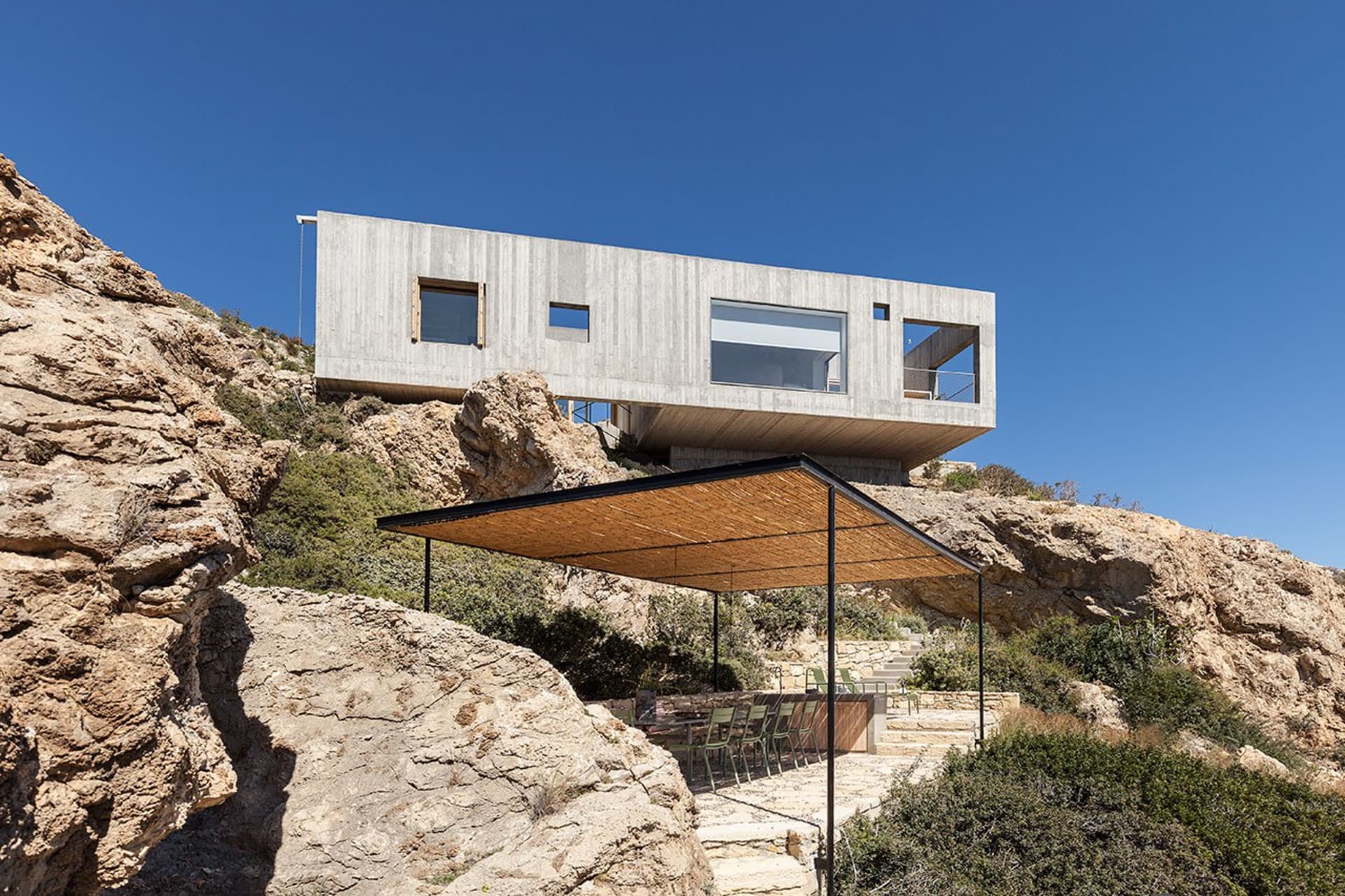 A modern residential architecture with a concrete structure and a roof-covered patio area.