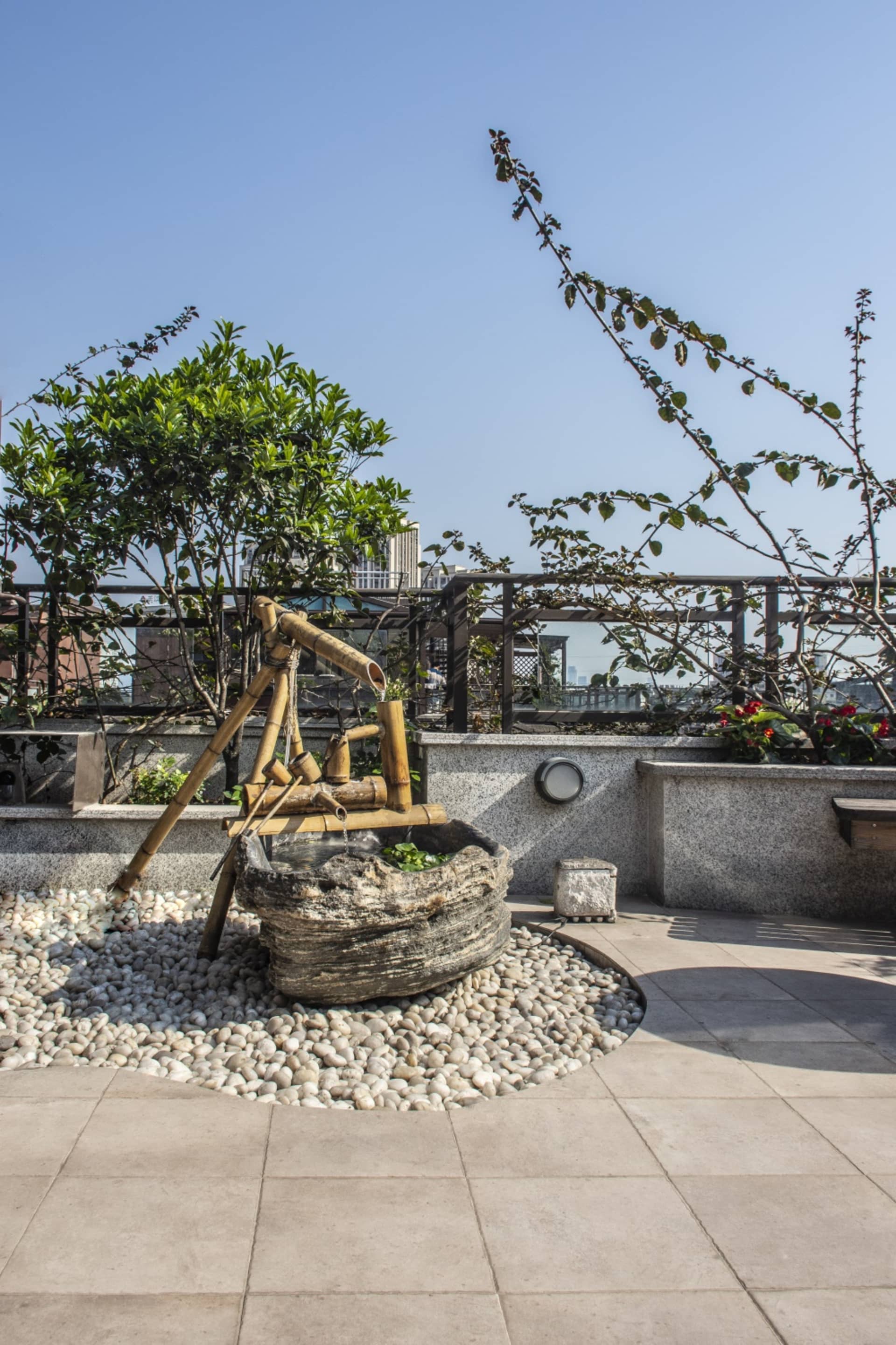 A serene outdoor space featuring a stone water bowl, bamboo water feature, and gravel pathway.