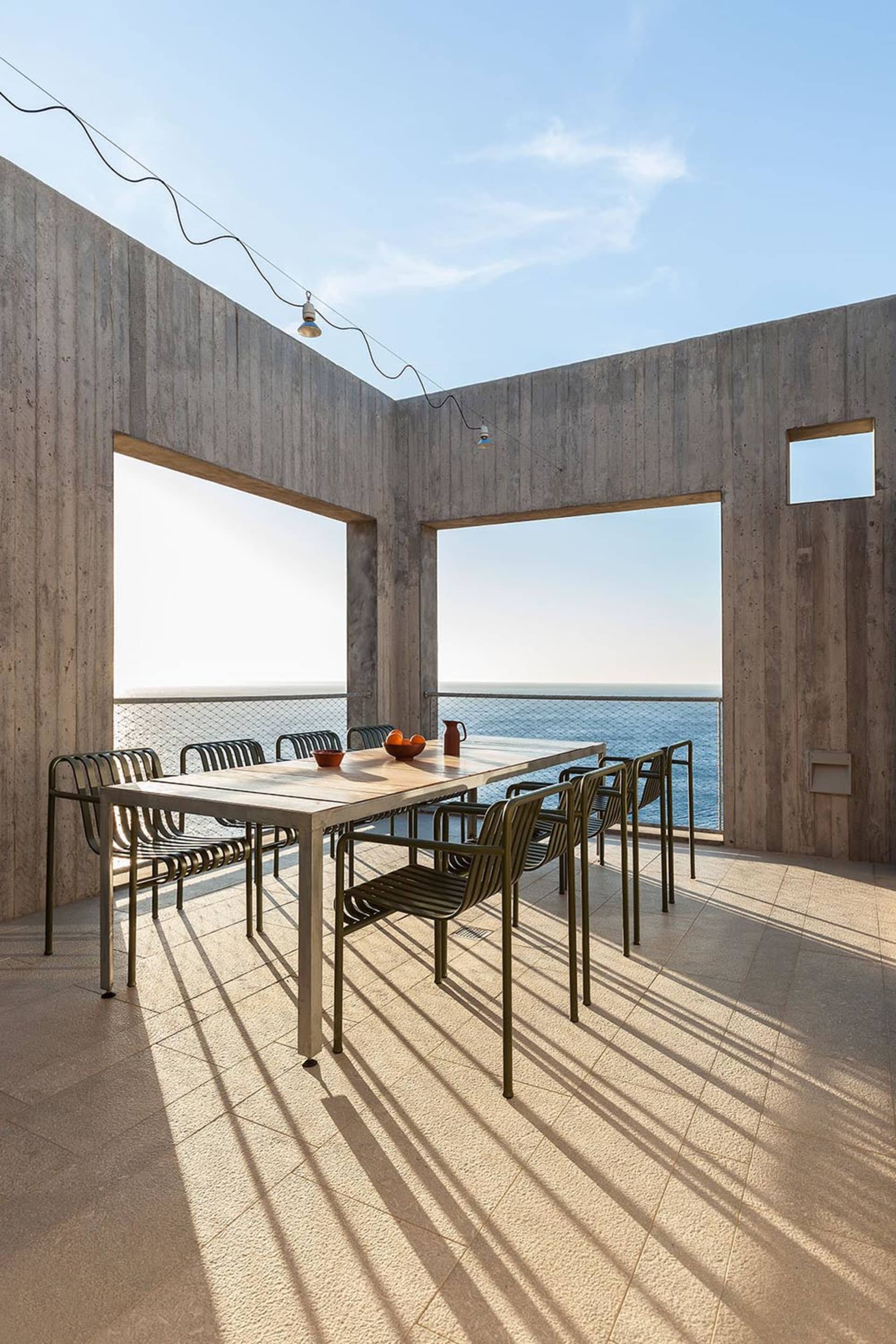 Contemporary patio area with concrete walls and metal chairs and table, featuring an ocean view.