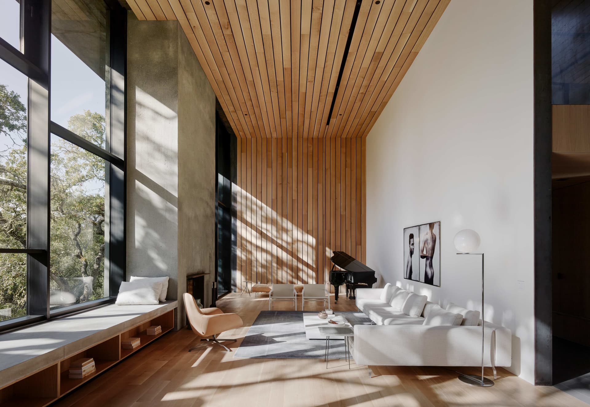 A modern living room with a white couch, wooden floor, concrete wall, and large windows showcasing a serene outdoor view.