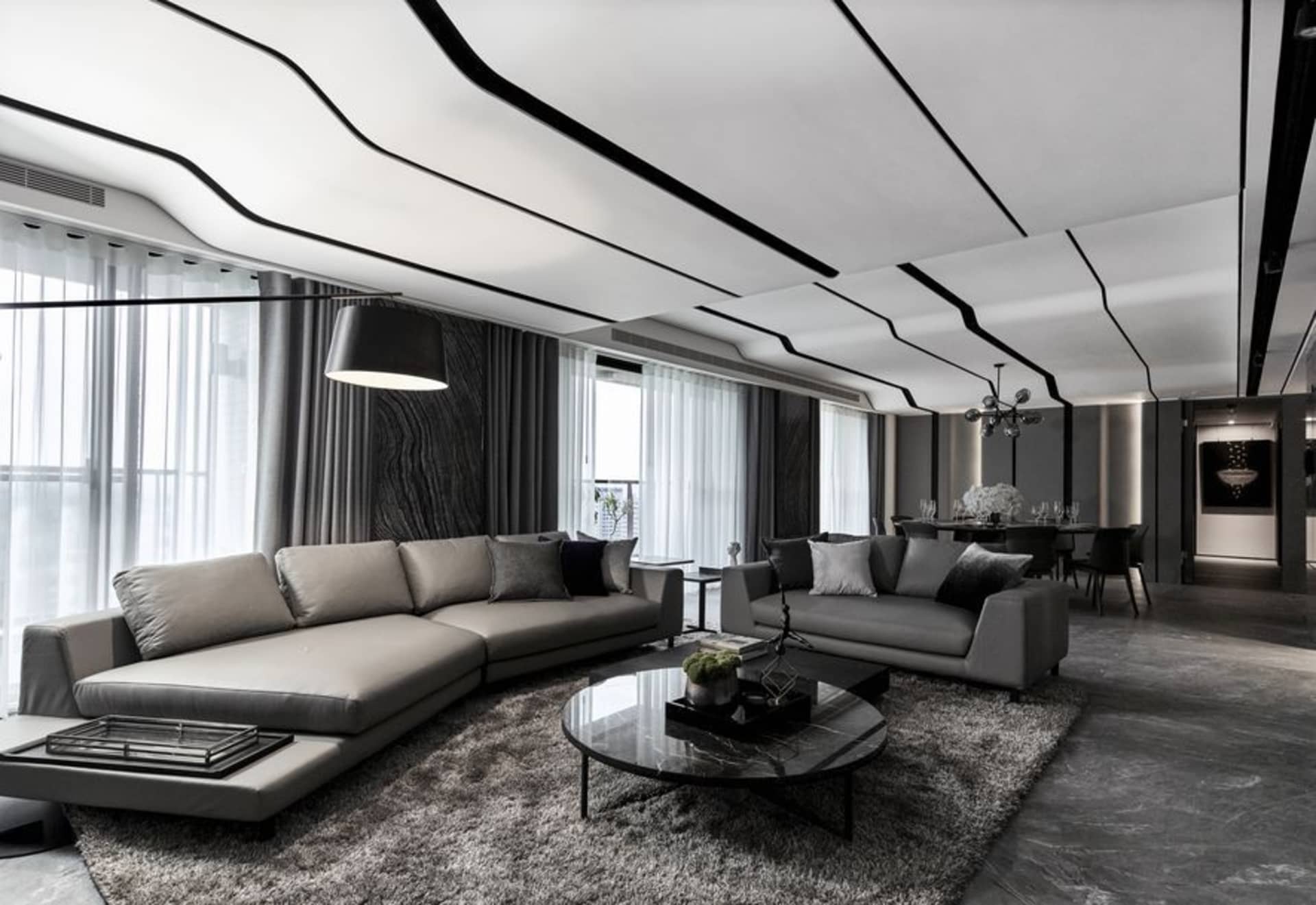 Modern minimalist living room featuring textured gray cement flooring, gray sofas, and an abstract black and white ceiling de