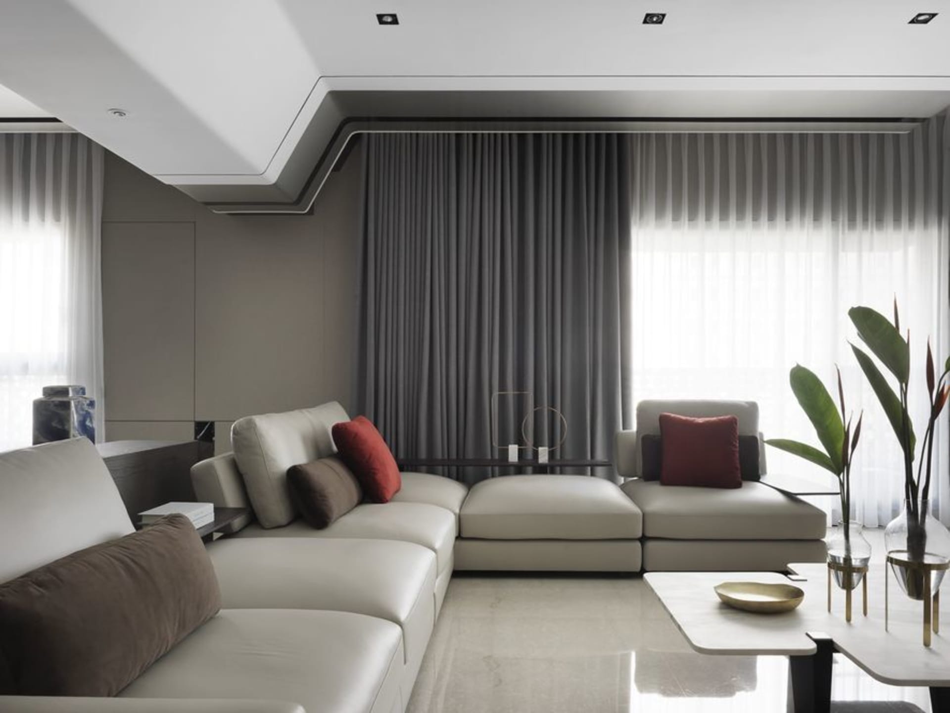 Modern minimalist living room with grey curtains, a white sectional sofa, and a coffee table with decorative items.