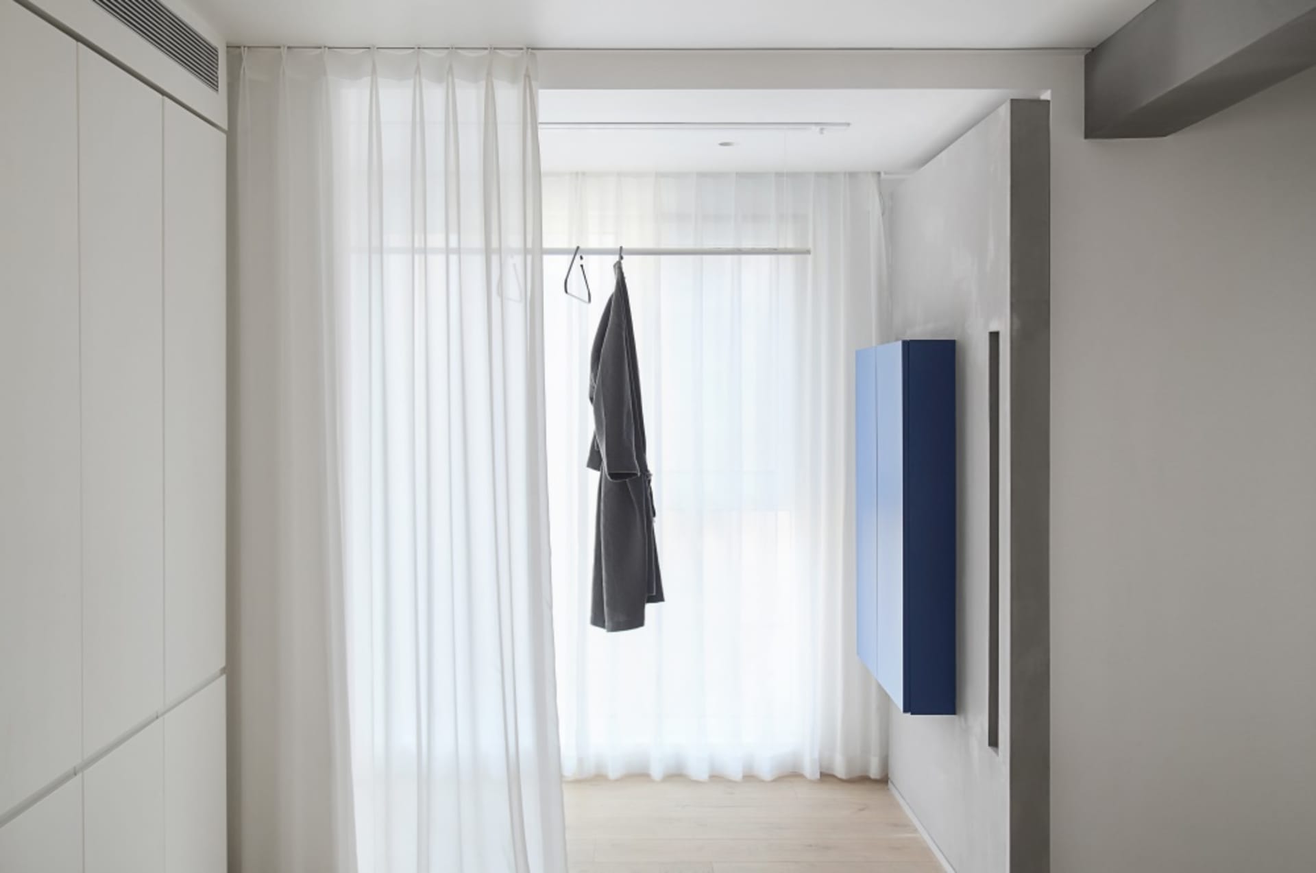 A minimalist closet area featuring white curtains and clothing storage.