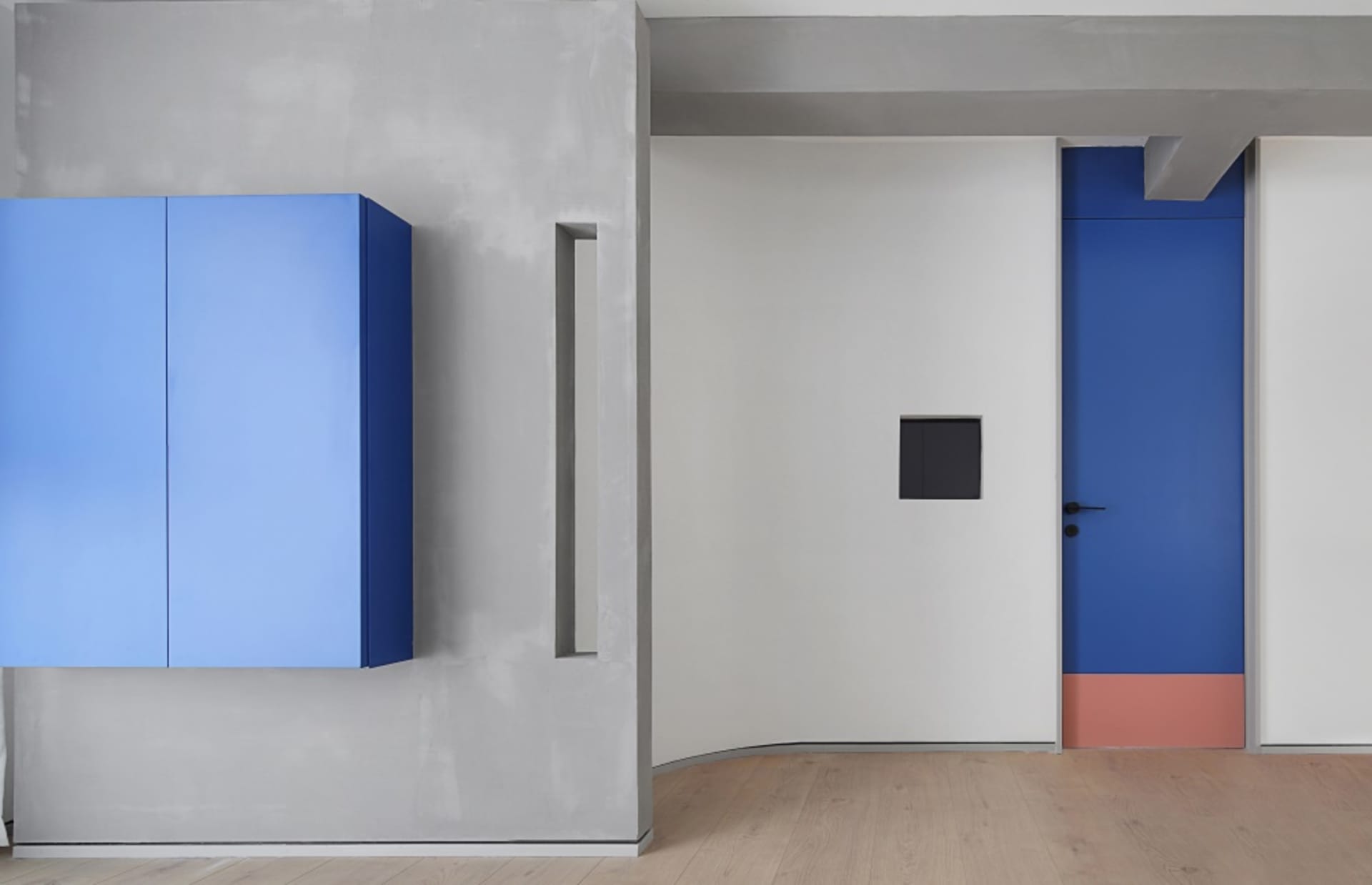 A minimalist interior with a blue-cabinet, light wooden floor, and a red and blue door with a black panel.