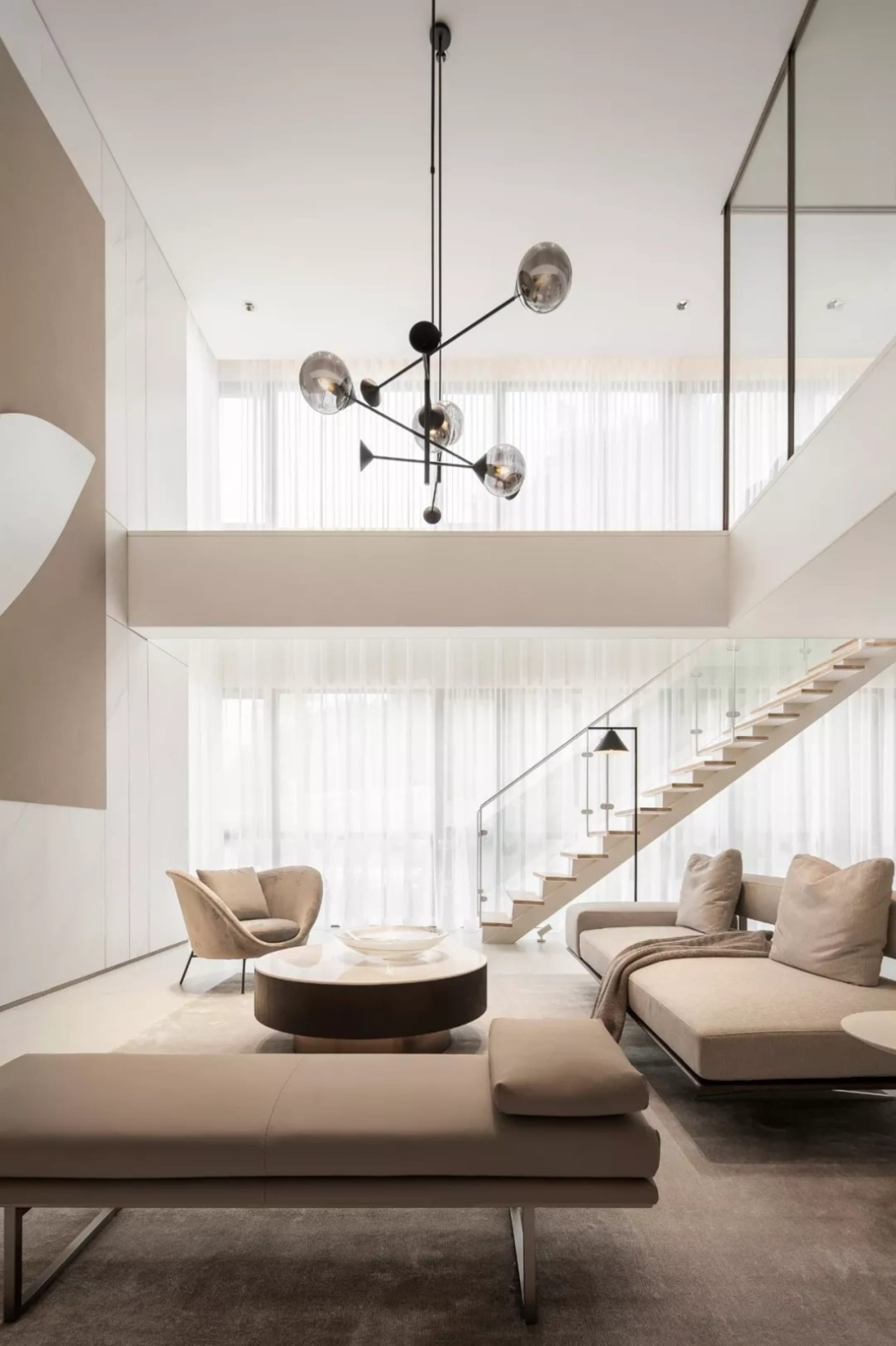 Modern minimalist living room with a glass staircase, beige seating, and a central coffee table.