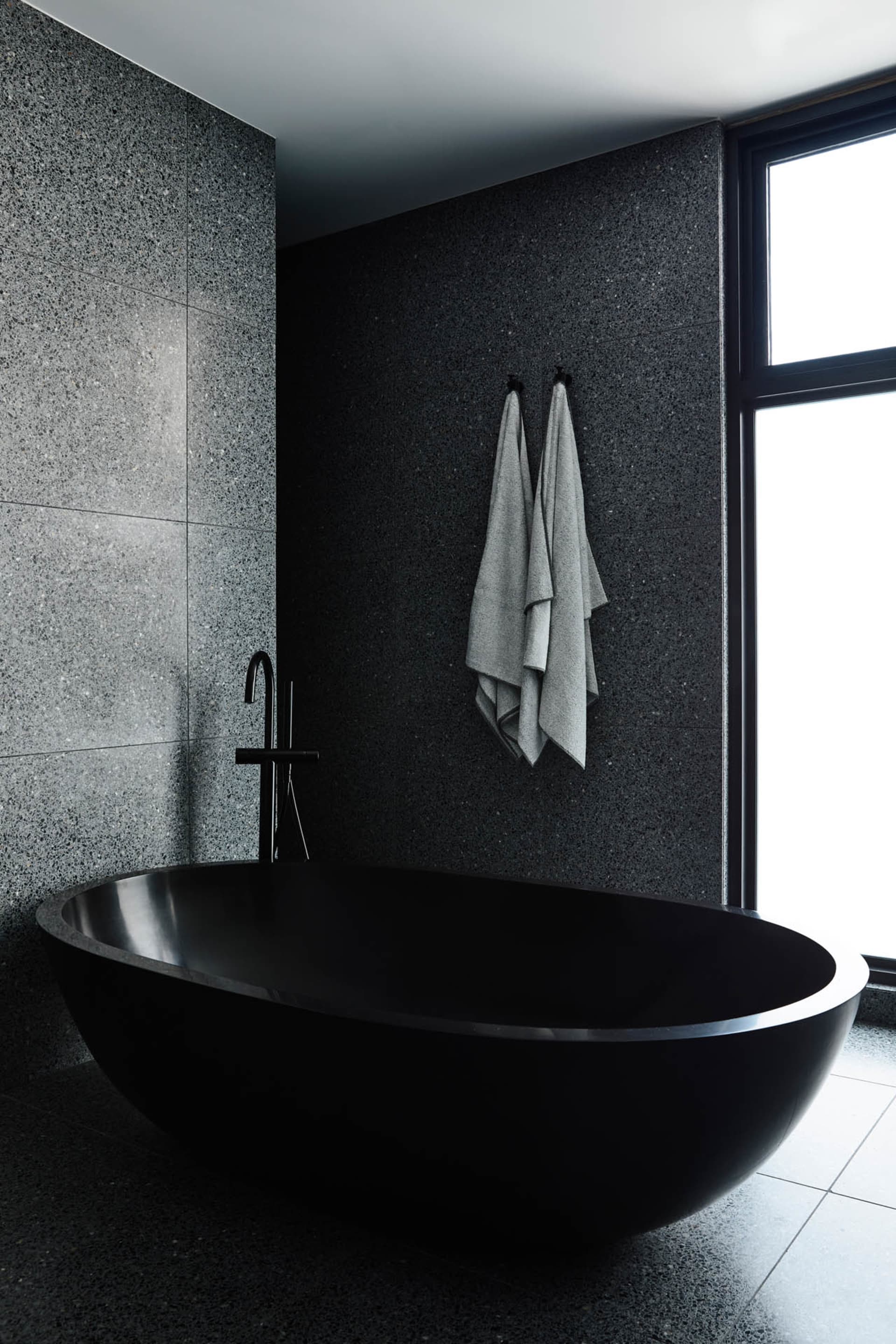 Modern minimalist bathroom featuring a sleek black bathtub made of marble.