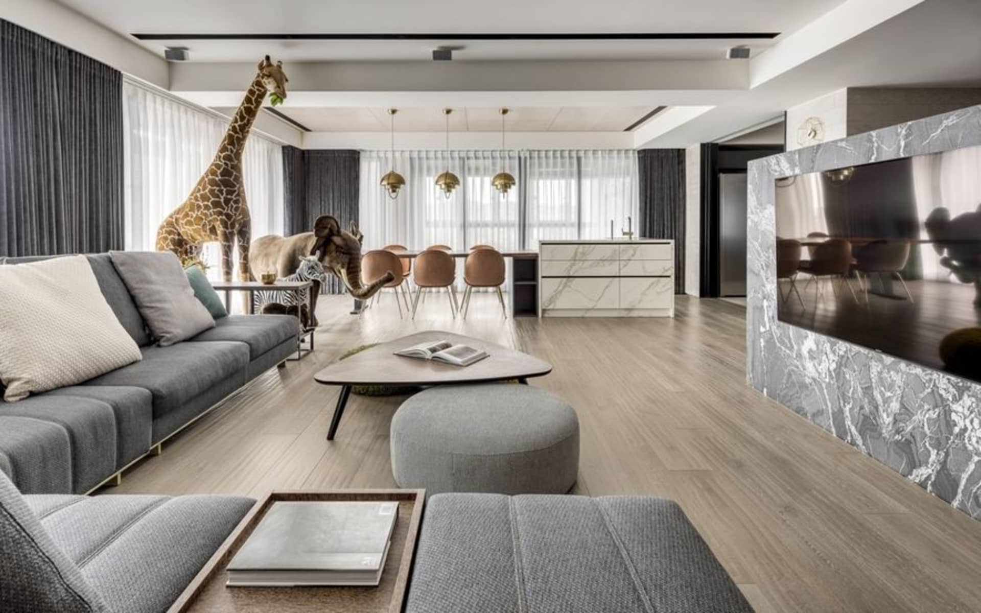 Modern living room featuring a dark grey sectional sofa, a round coffee table, a marble kitchen counter, and a large flat-scr