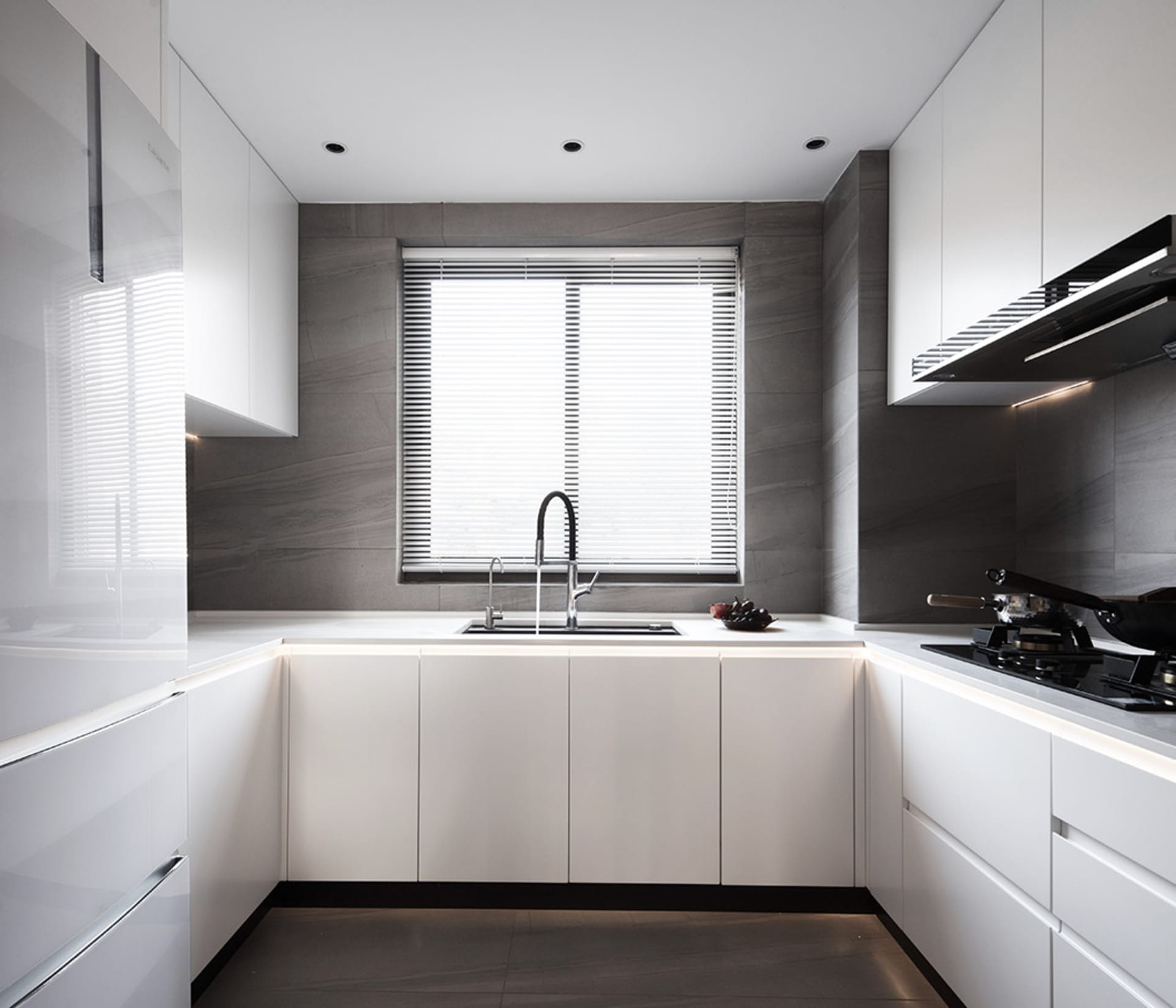 A modern minimalist kitchen with white cabinets and gray marble tile countertops, featuring a sleek sink and contemporary app
