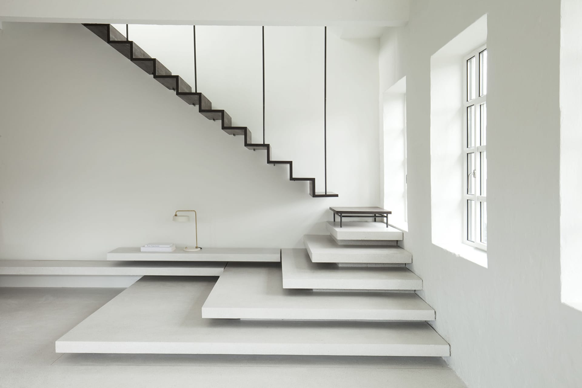 Modern minimalist interior design featuring a concrete staircase with floating steps and a simple, elegant lamp.
