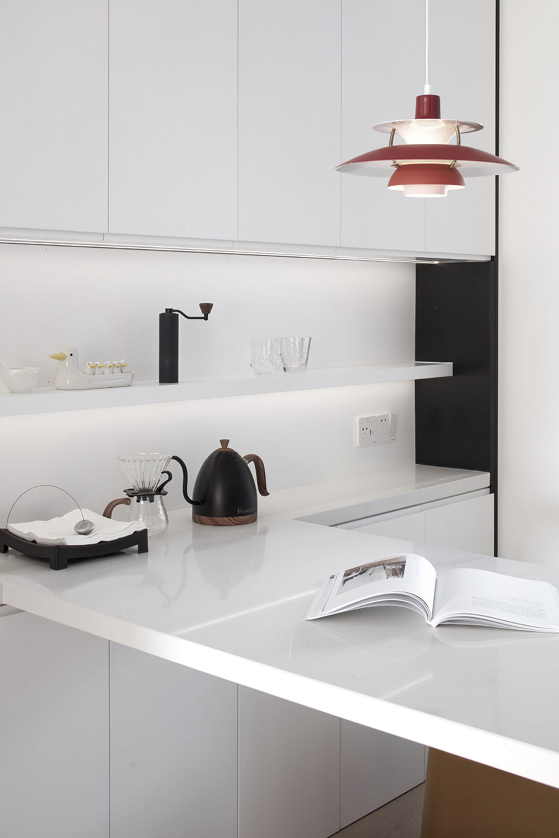Modern minimalist kitchen with sleek white marble countertops and cabinets, featuring a minimalist pendant light fixture.