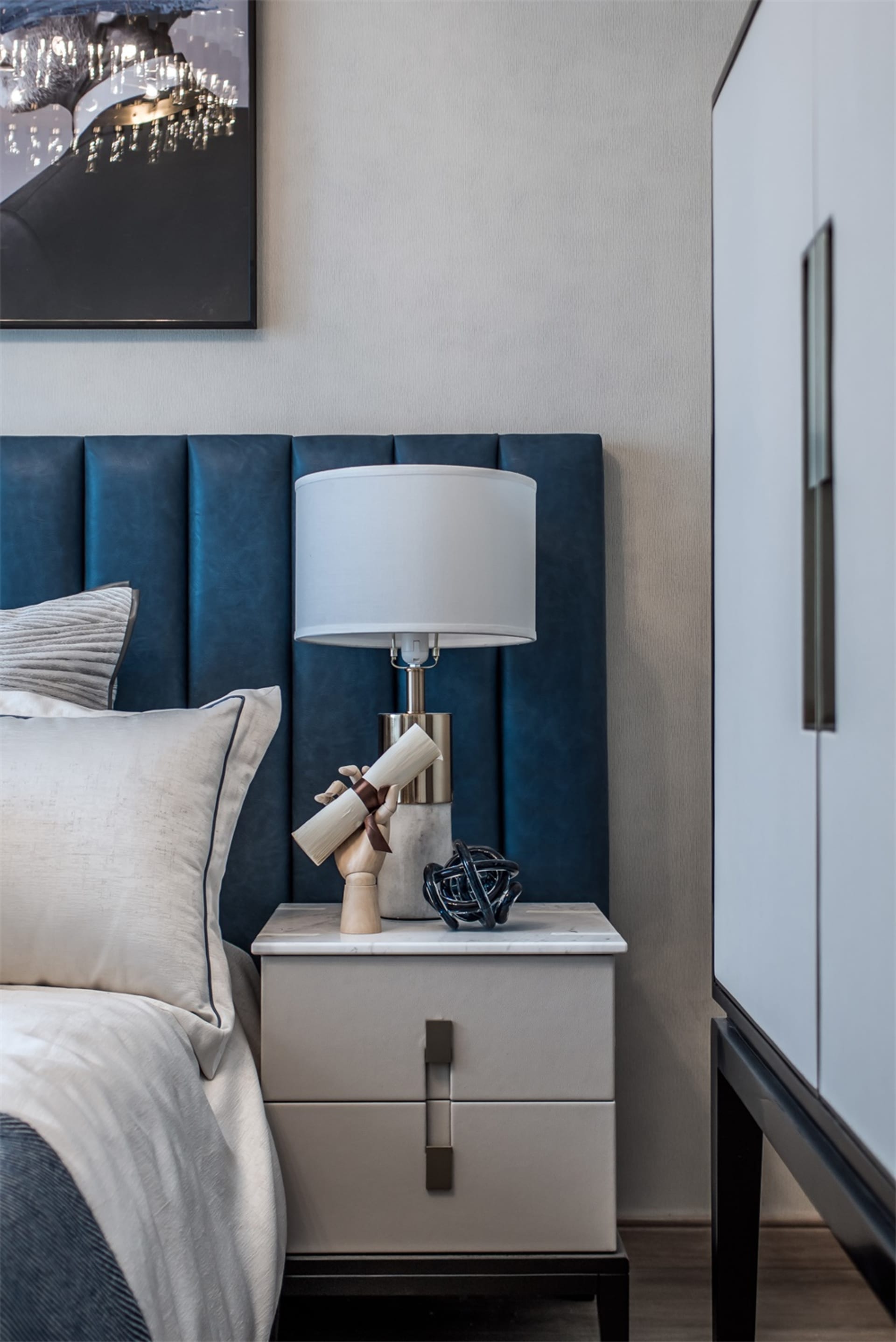 Modern bedroom with a blue upholstered bed, white nightstand, and marble lamp base.