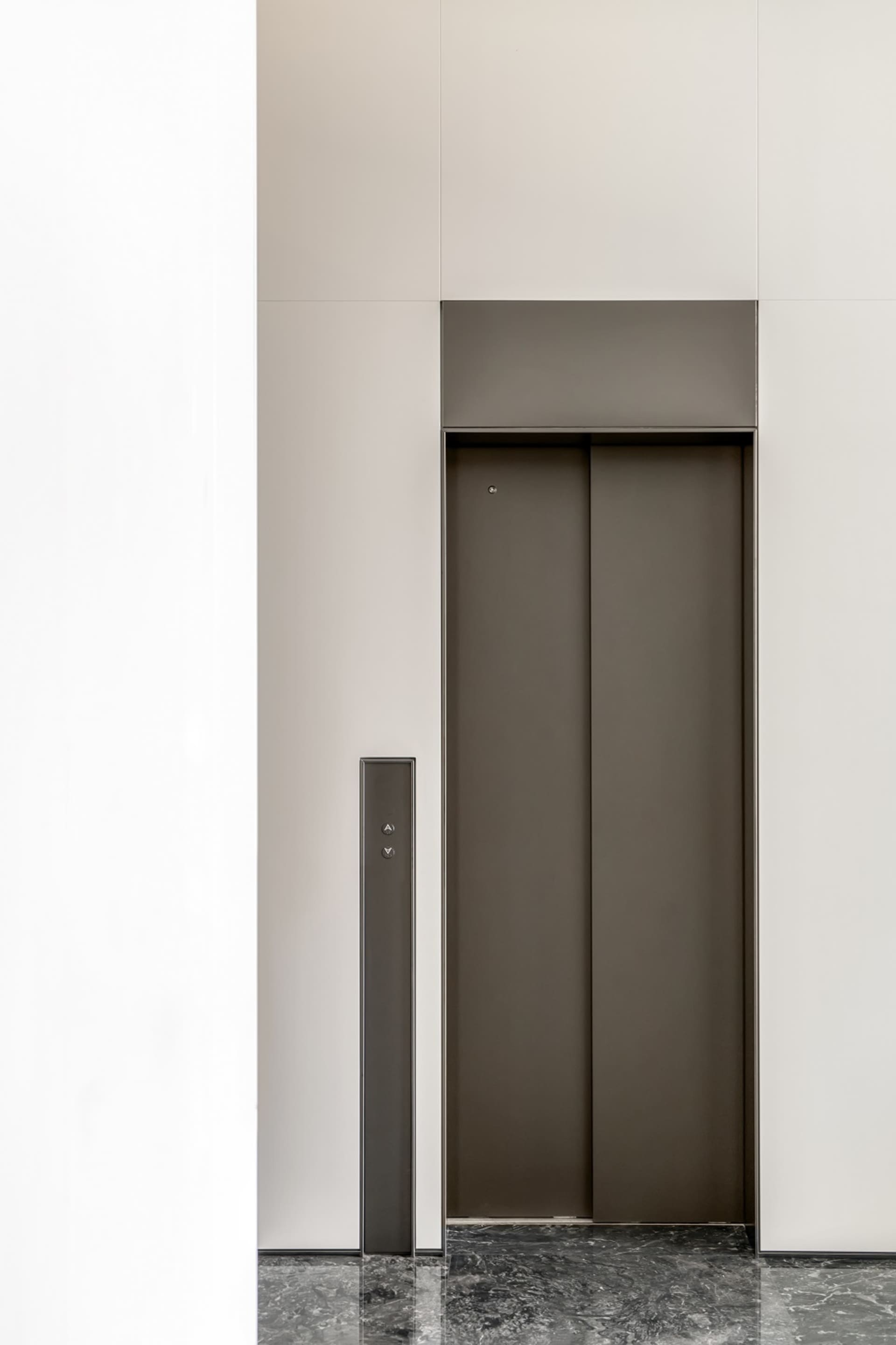 A modern elevator interior featuring black metallic doors on a minimalist white wall.