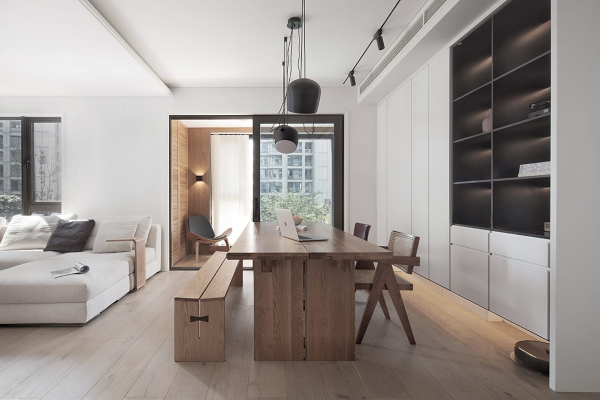 A modern living room featuring a contemporary sofa, large windows, minimalist design, and a natural wood dining table.