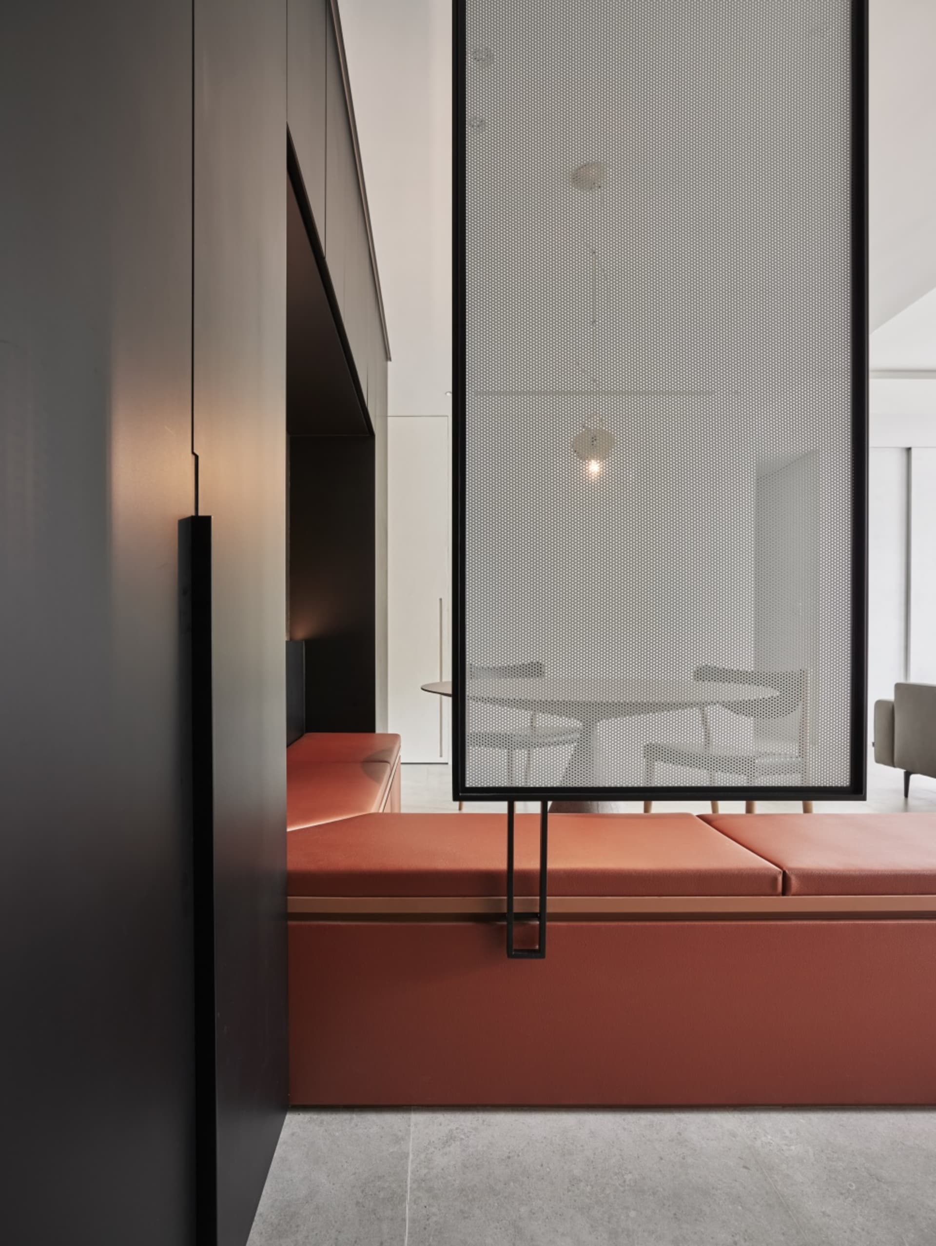 Detailed view of a modern living space featuring a metal perforated panel wall, orange seating, and white furnishings.