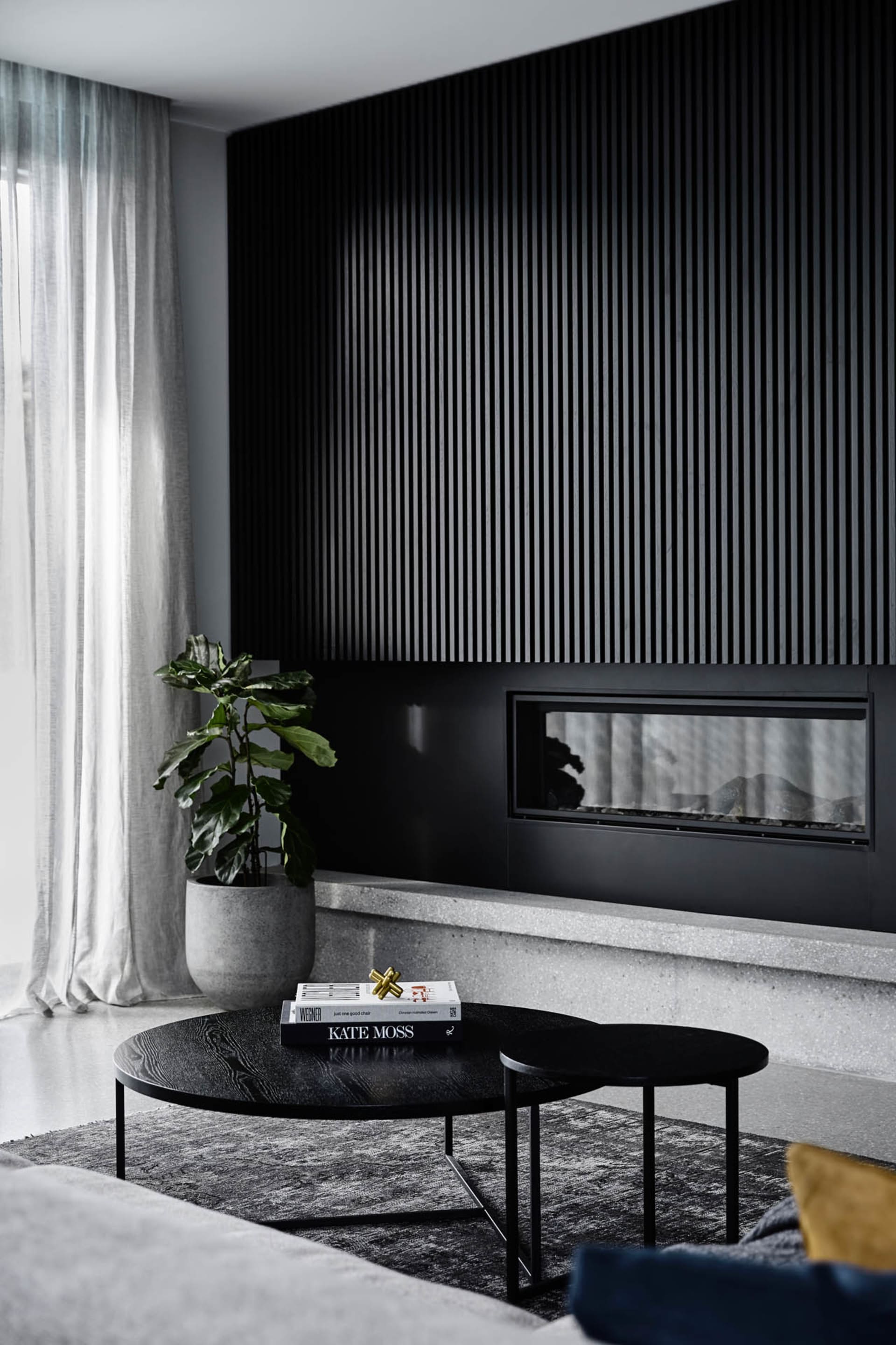 A modern minimalist living room with a dark accent wall, concrete floor, and wood coffee table.