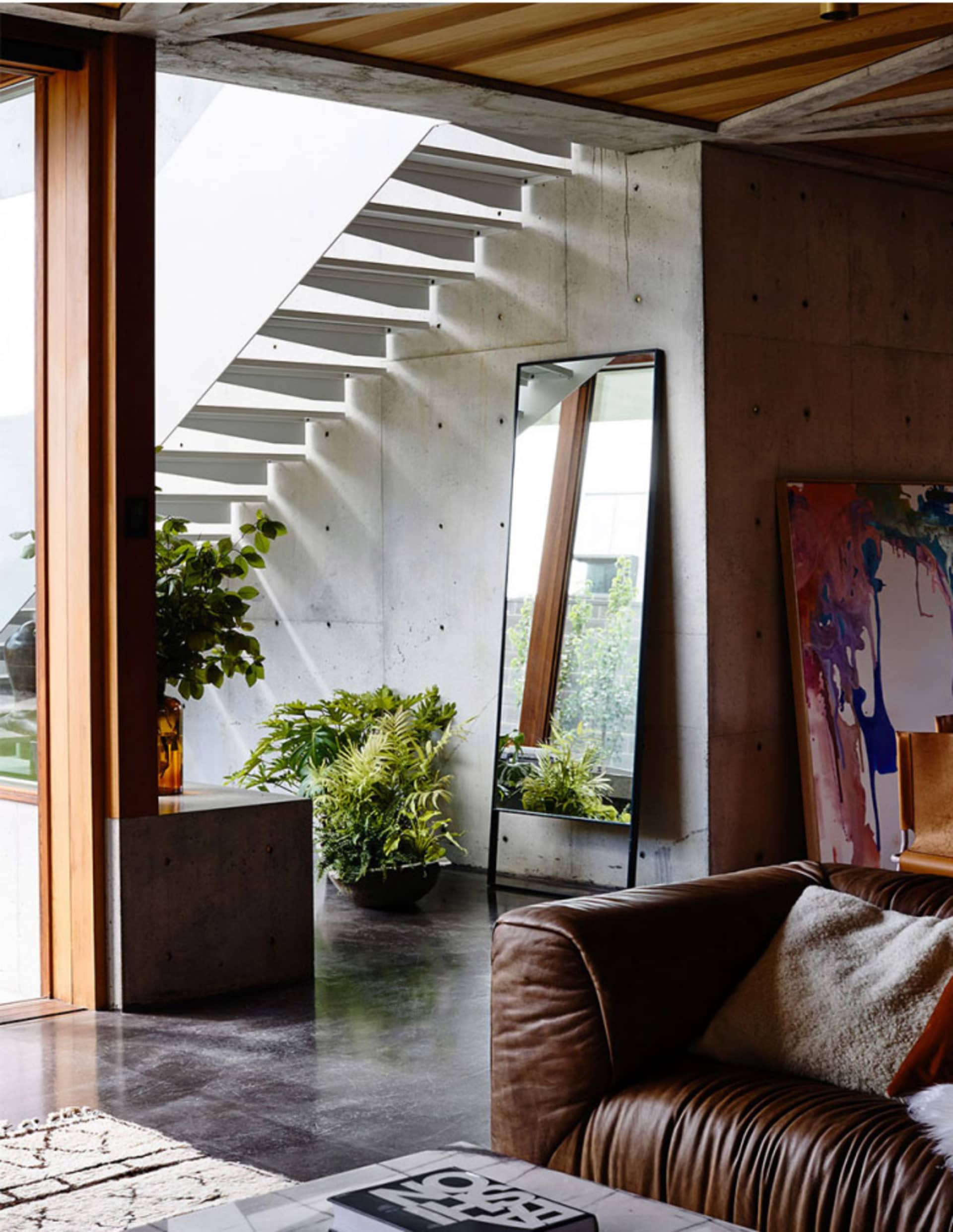 Modern minimalist living room featuring a concrete staircase and a brown leather sofa.