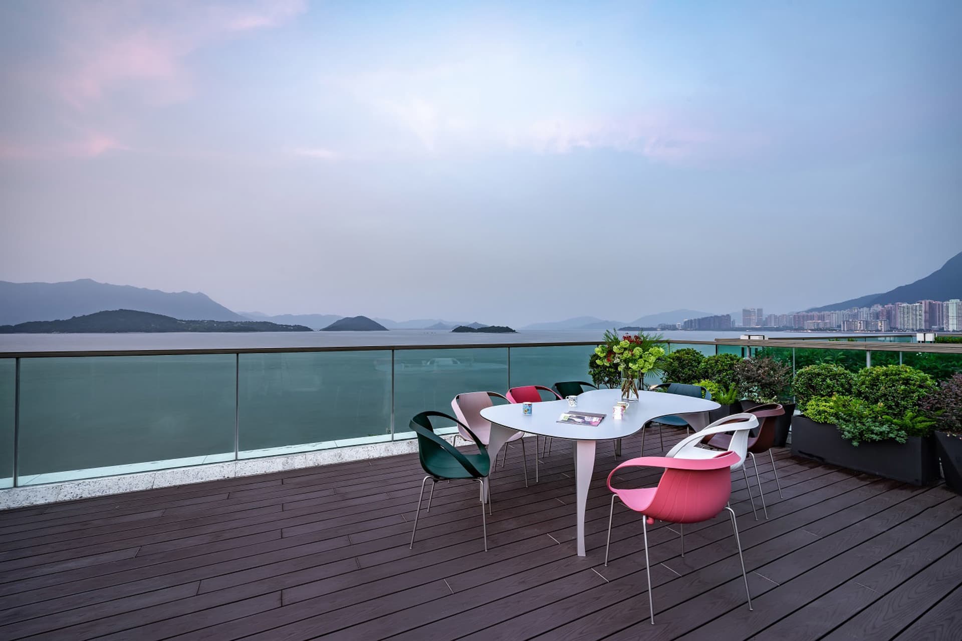 A modern rooftop deck with colorful chairs and a table overlooking a scenic landscape.
