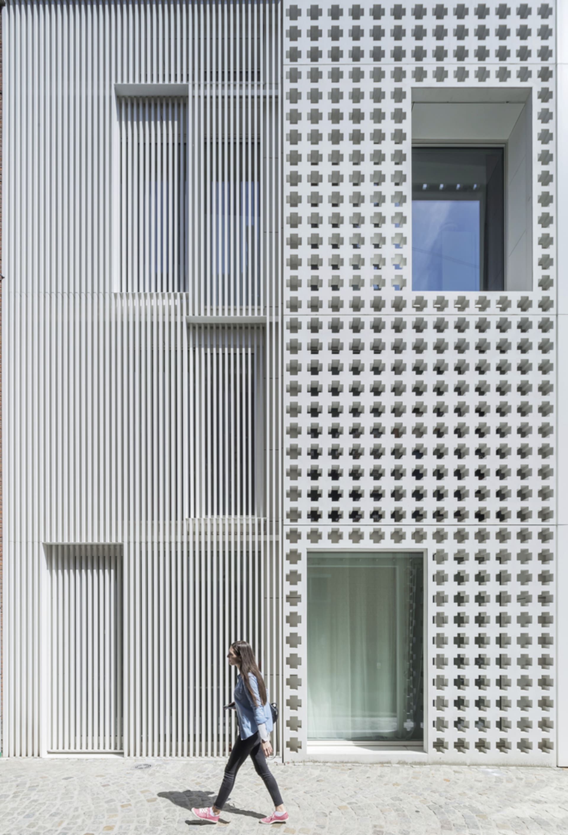 Person walking past a modern building with concrete texture and geometric patterns on the facade.