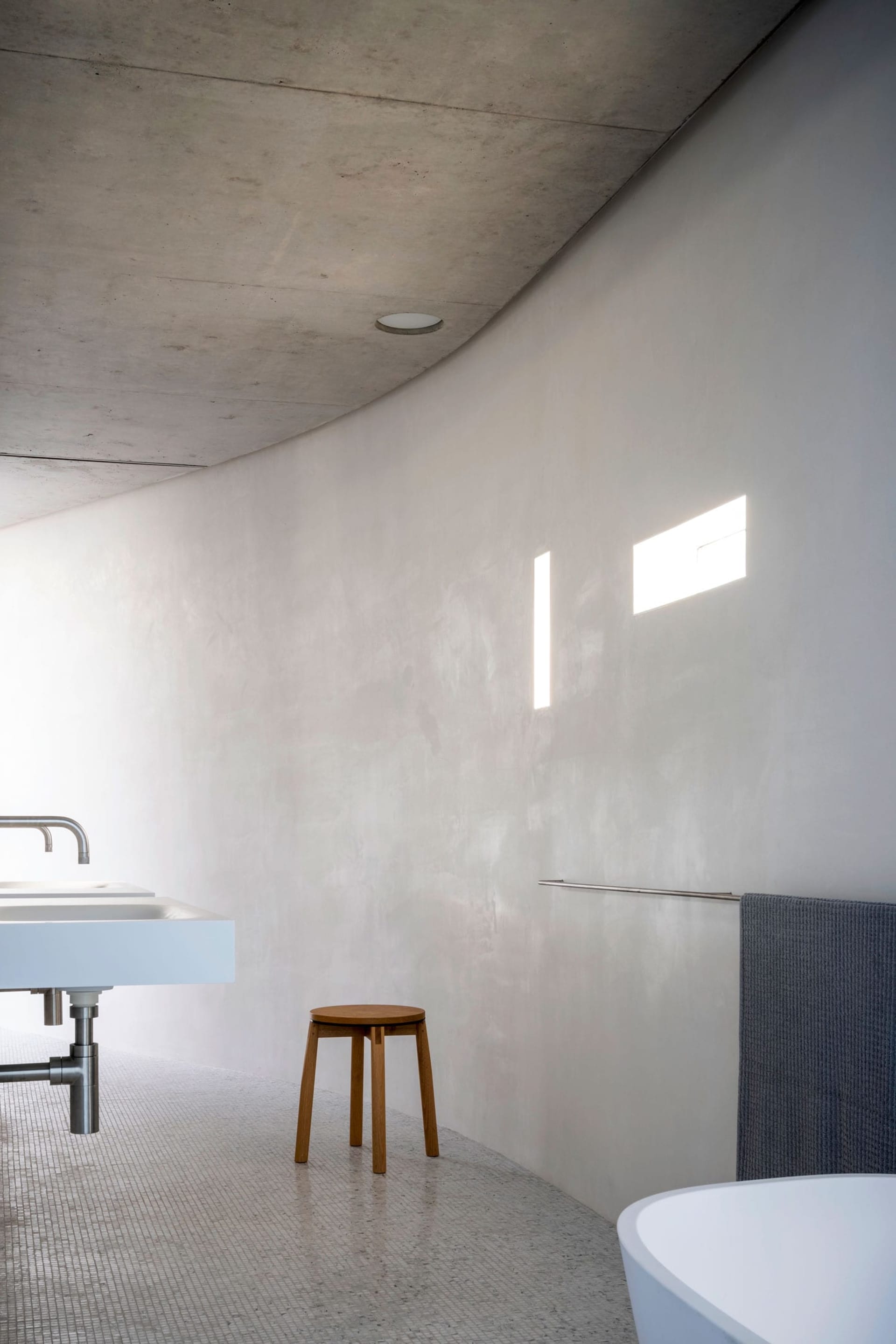 A modern bathroom with a concrete wall, minimalistic design, and a stool.
