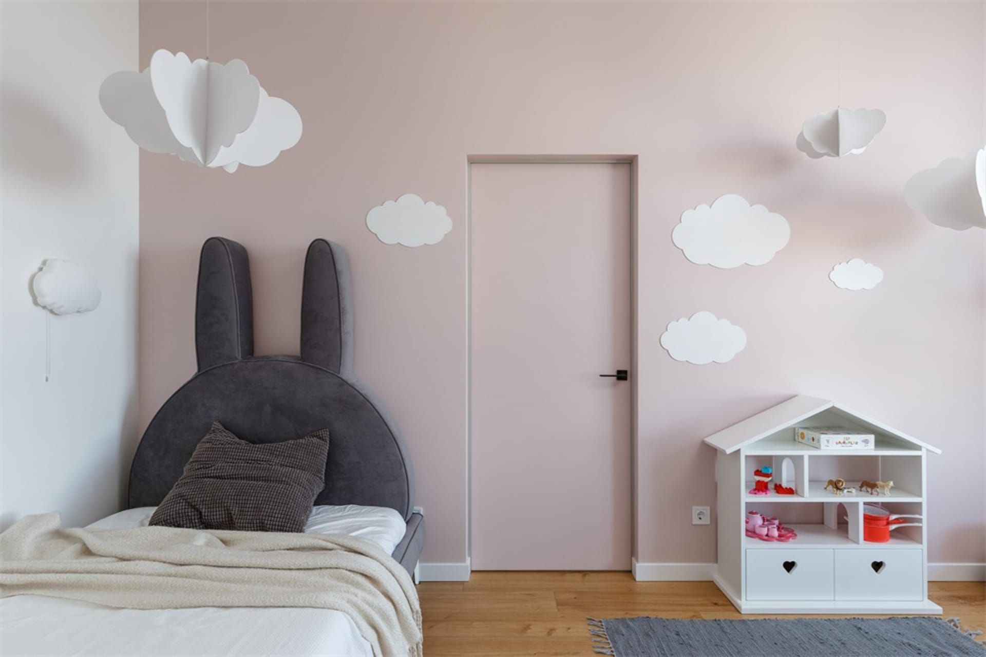 A modern children's bedroom with a fabric headboard designed like bunny ears, white clouds hanging from the ceiling, and a sm