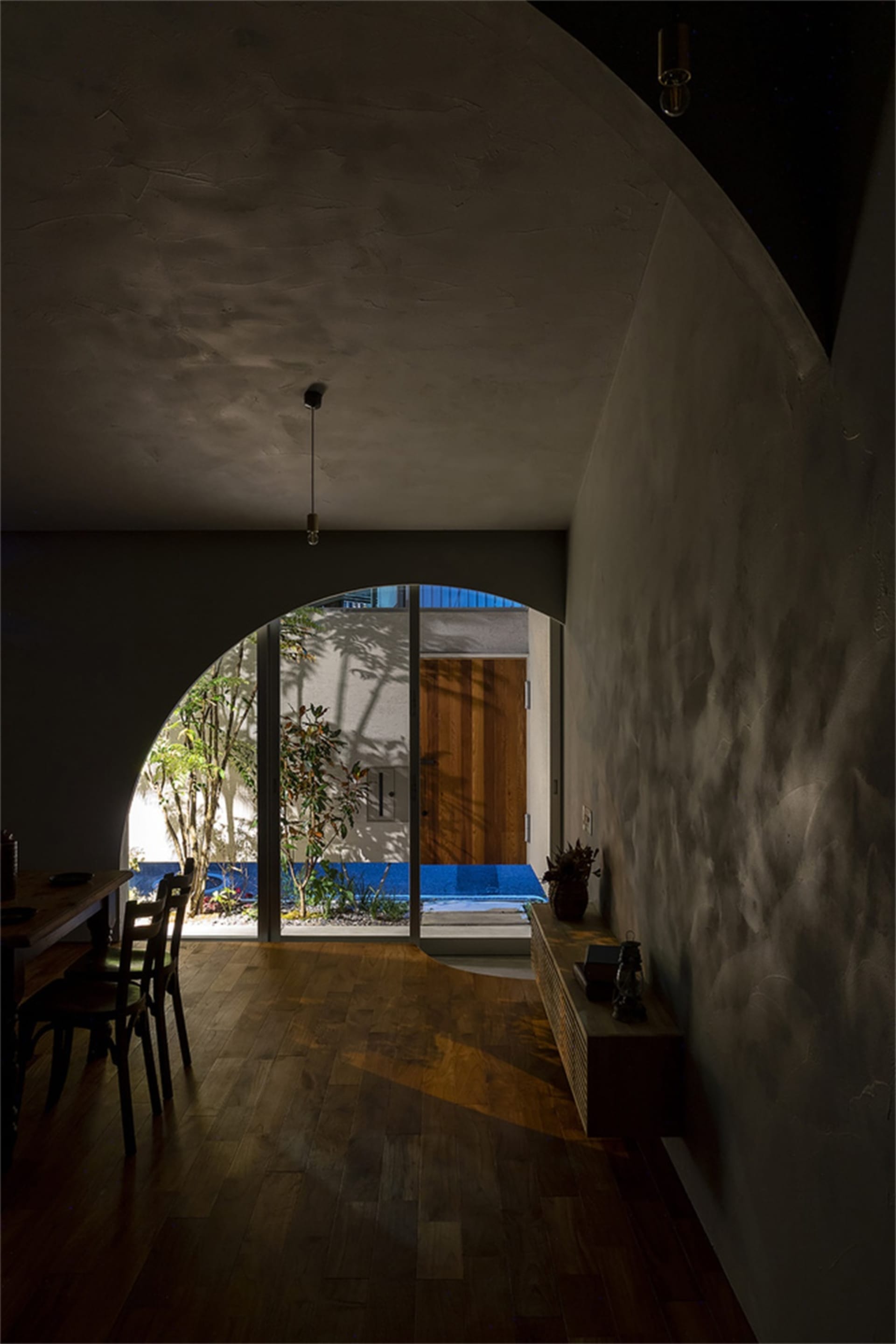 A spacious, modern interior with concrete walls and wooden flooring, featuring a dining area and a view through an archway to