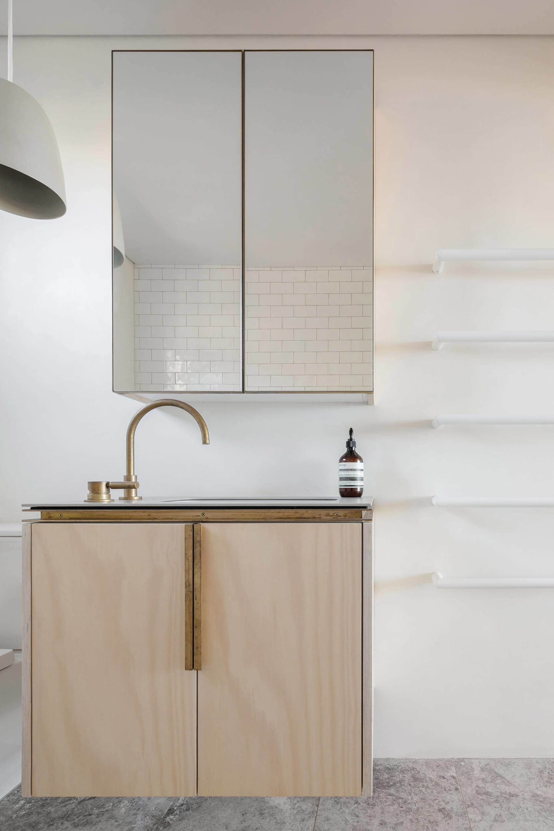 A modern minimalist bathroom featuring a wooden cabinet with a brass faucet and a white tiled wall.