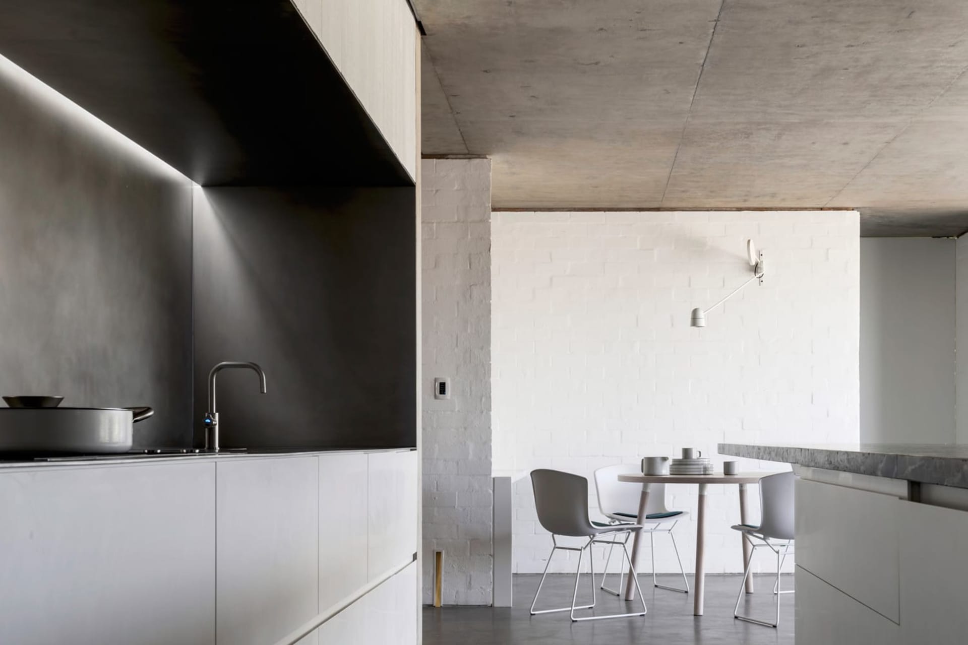 Modern kitchen with minimalist design, featuring concrete countertops and white fixtures.