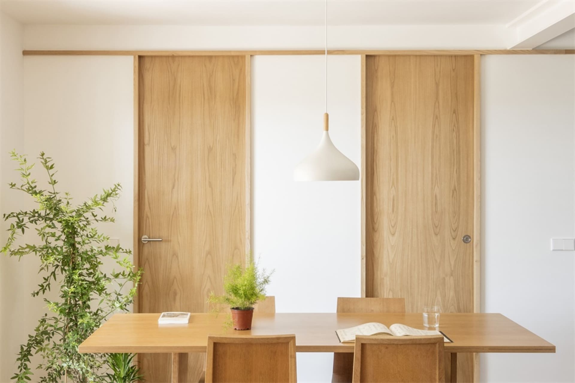 Interior of a modern minimalist dining room featuring a wooden table, chairs, and pendant lamp.