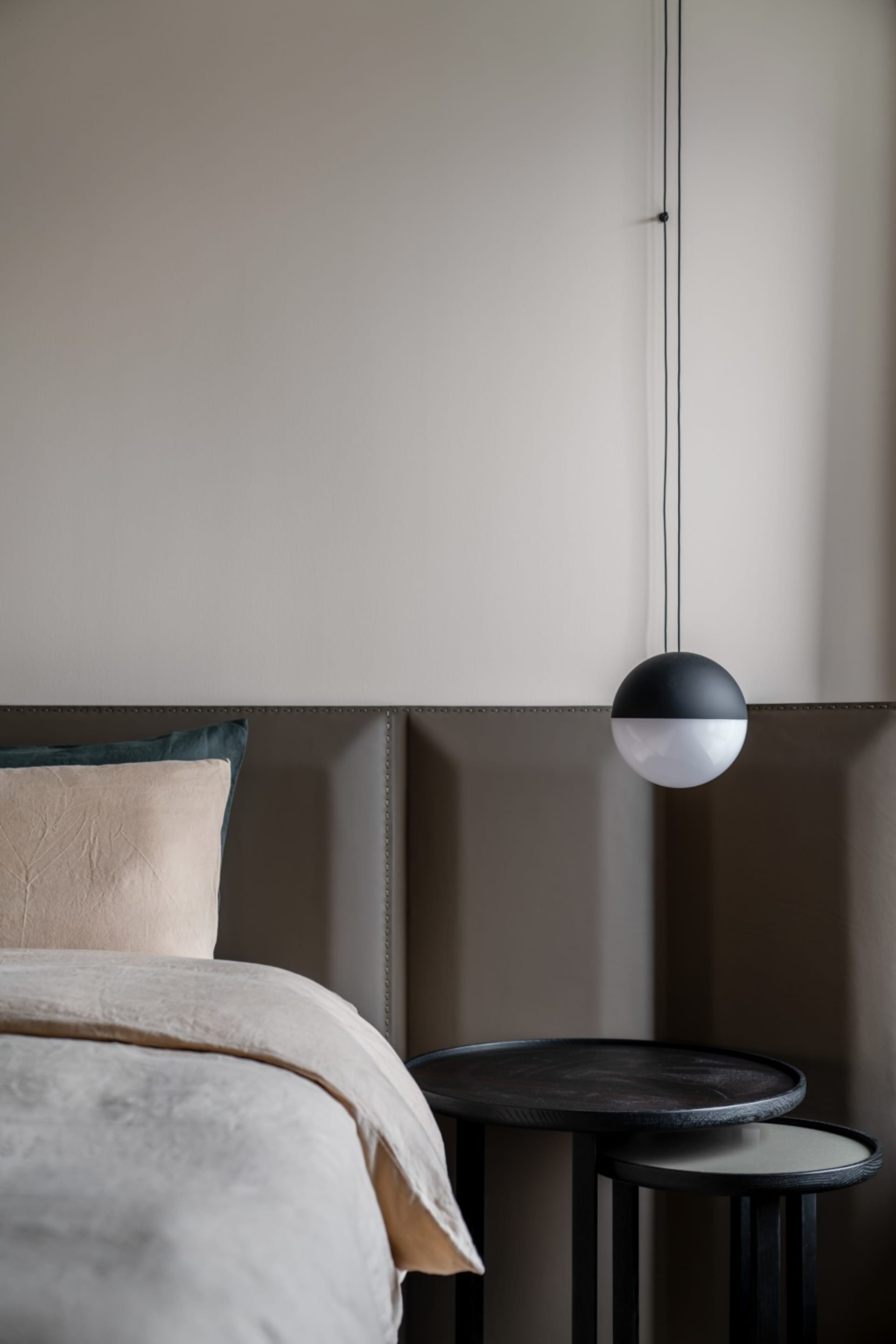 Modern minimalist bedroom with a neatly made bed featuring light-colored bedding, a hanging light fixture, and fabric-paneled