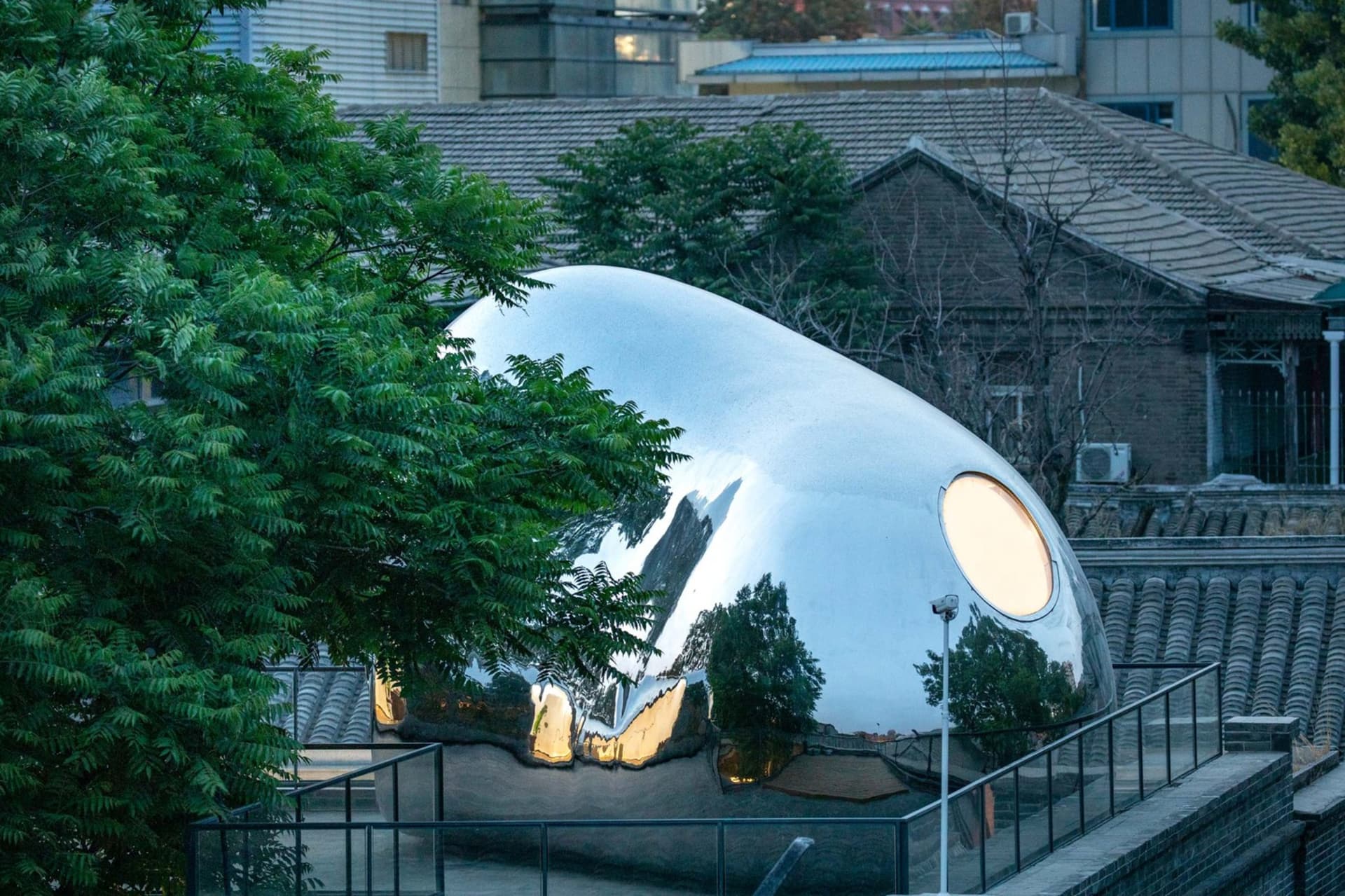 A minimalist metal sculpture with a smooth, polished surface and a circular window.