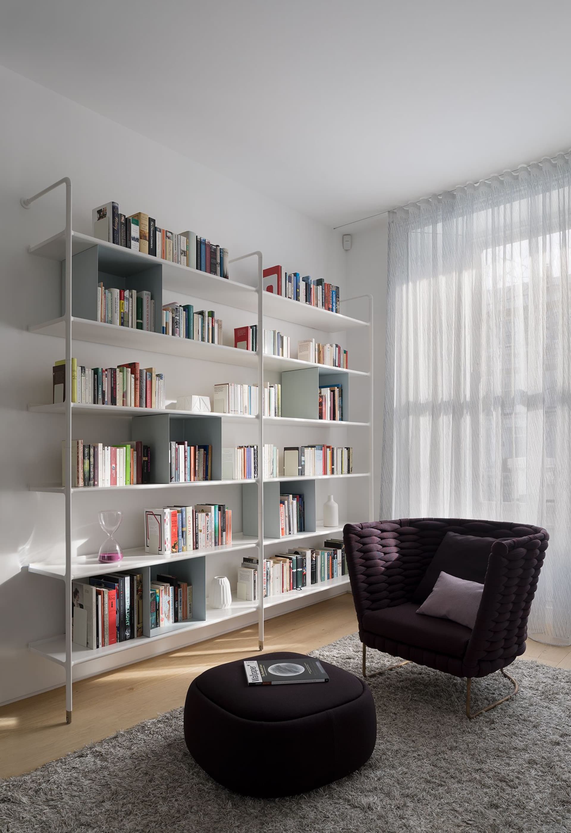 Modern living room featuring a minimalist white bookshelf with a cozy dark furniture piece and a plush ottoman.