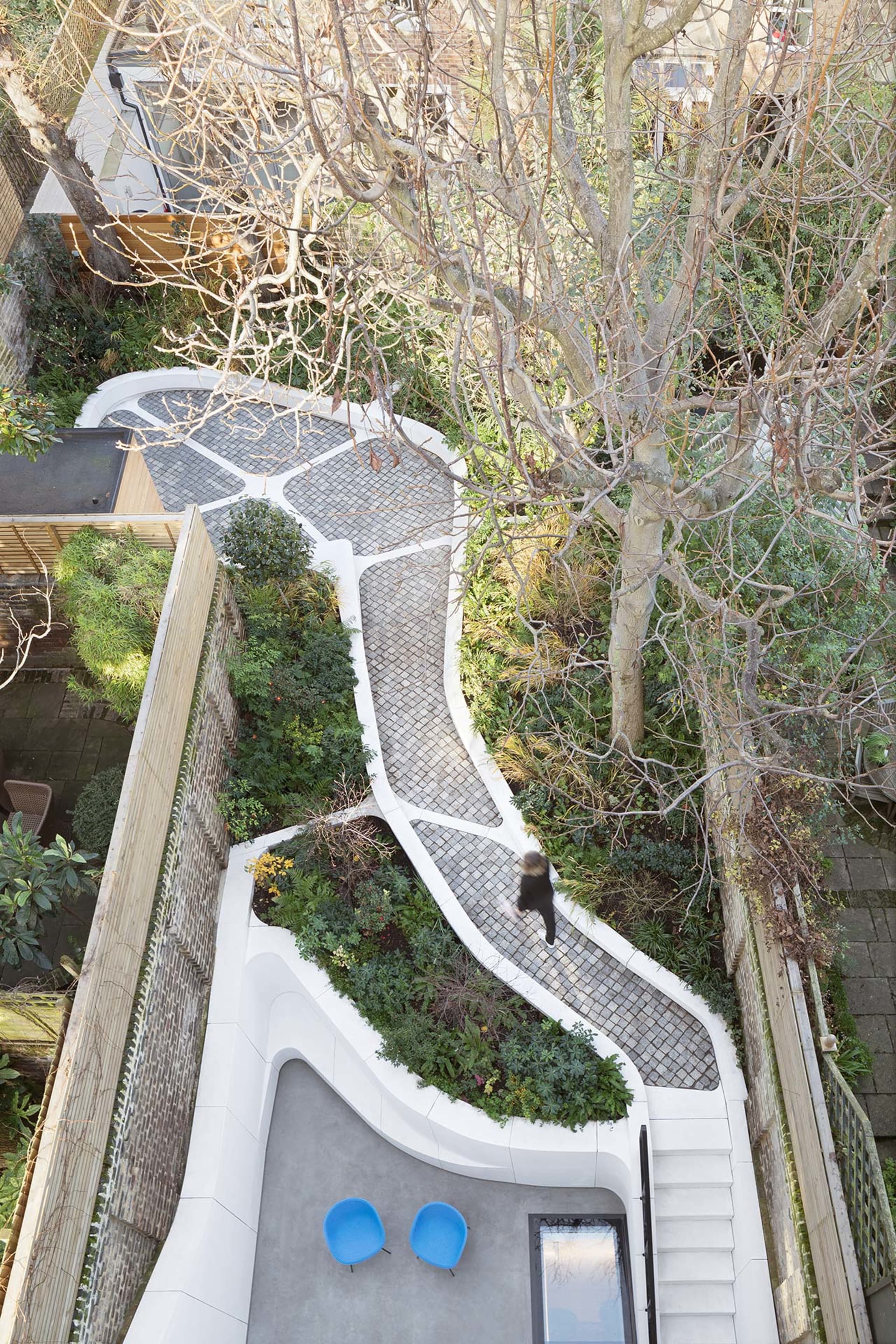 A modern garden pathway with stone-paving, surrounded by greenery and trees.